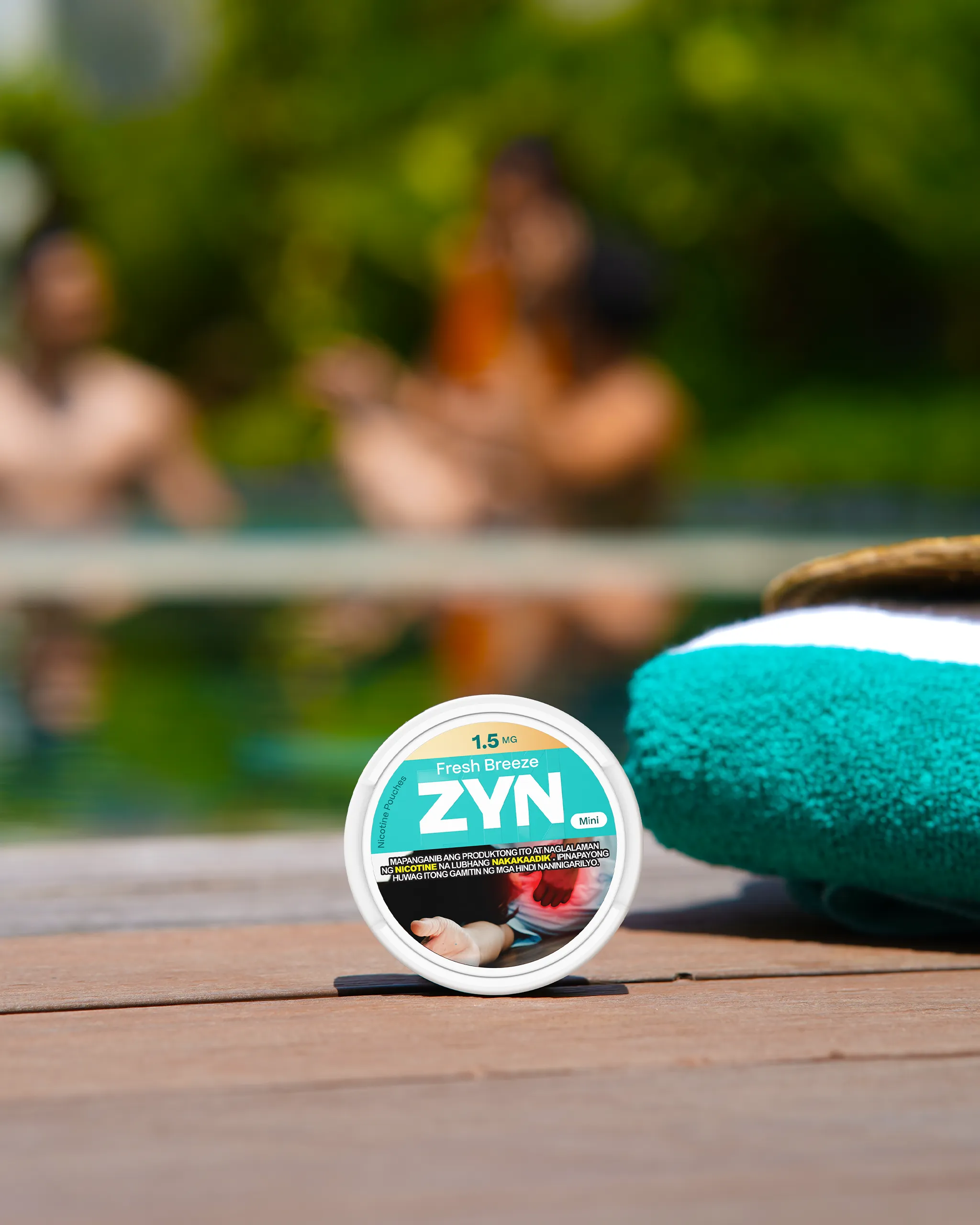 Close-up of a ZYN Fresh Breeze nicotine pouches can on a wooden surface with a blurred poolside scene in the background.