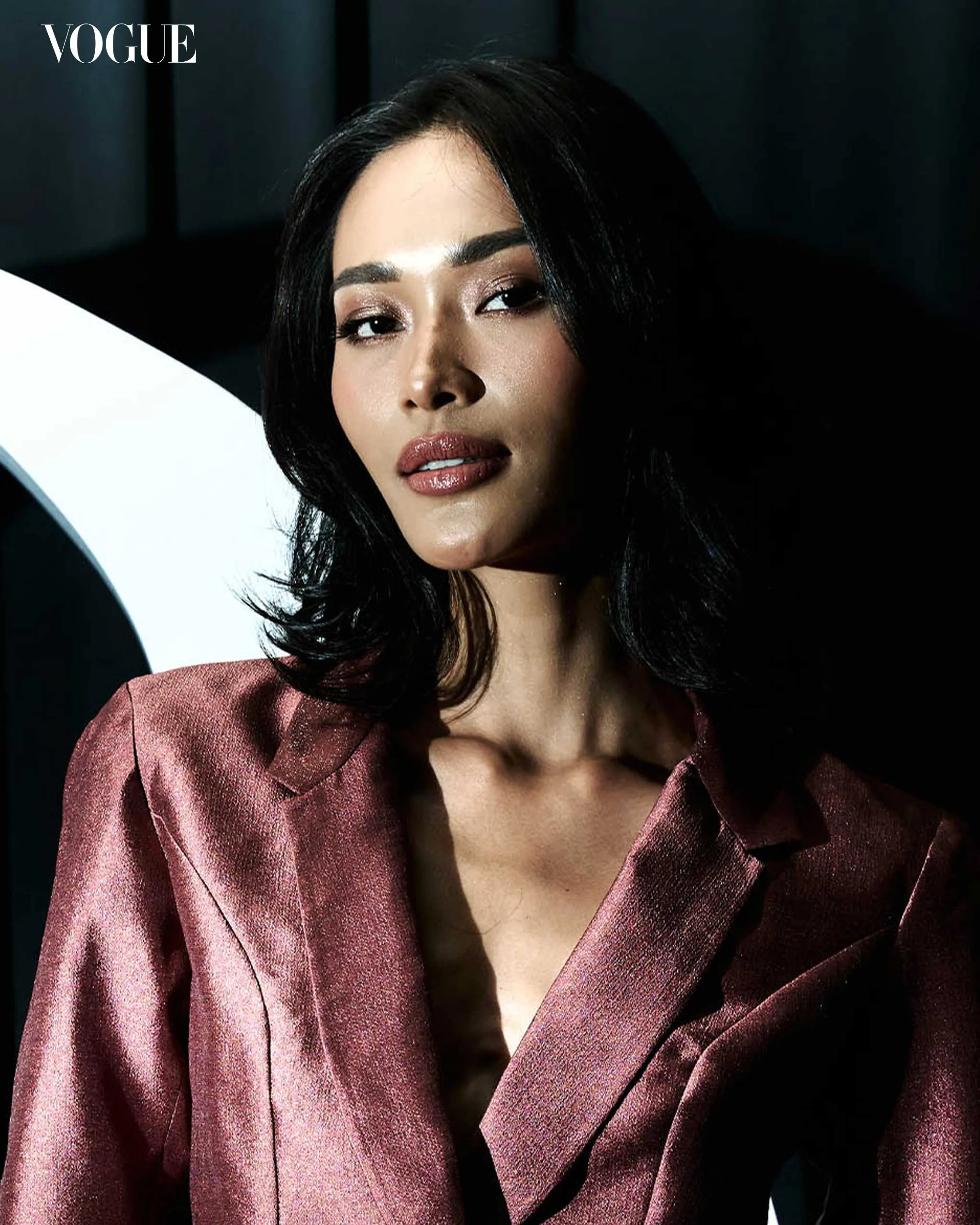 Model in a metallic pink blazer posing in studio light with Vogue logo in the top-left corner.