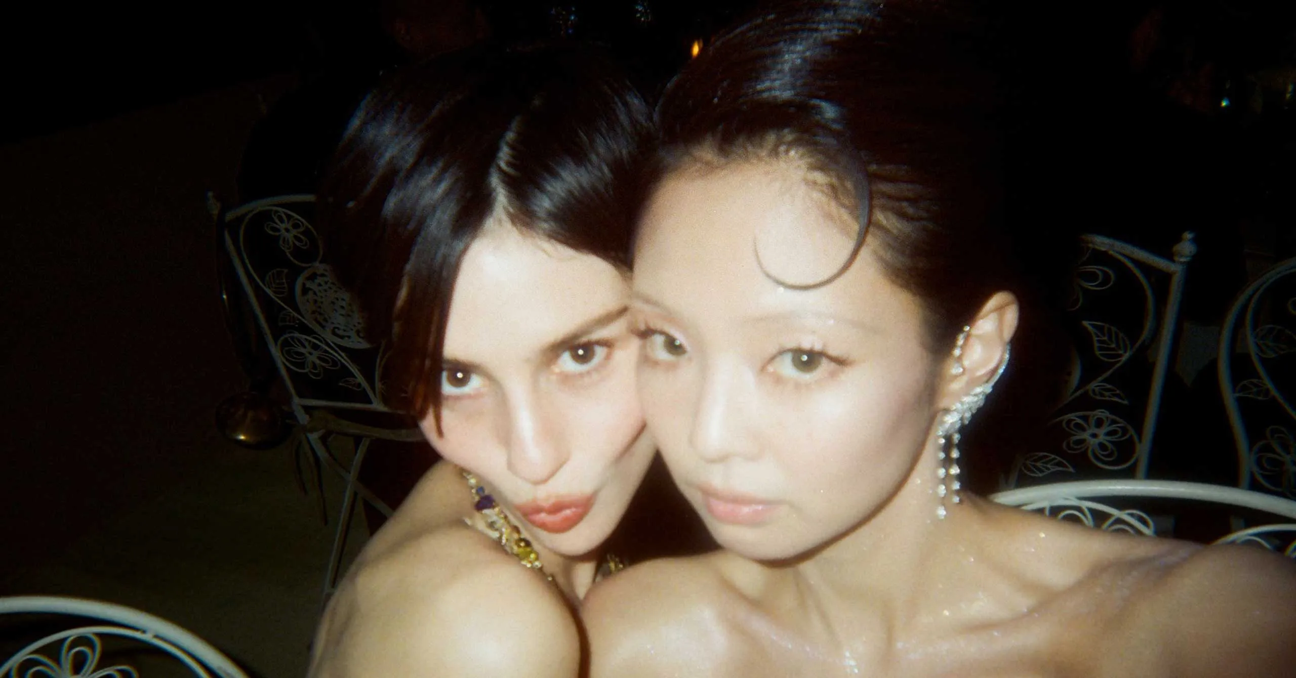 Two women posing closely for a nighttime selfie, smiling at the camera with jewelry visible