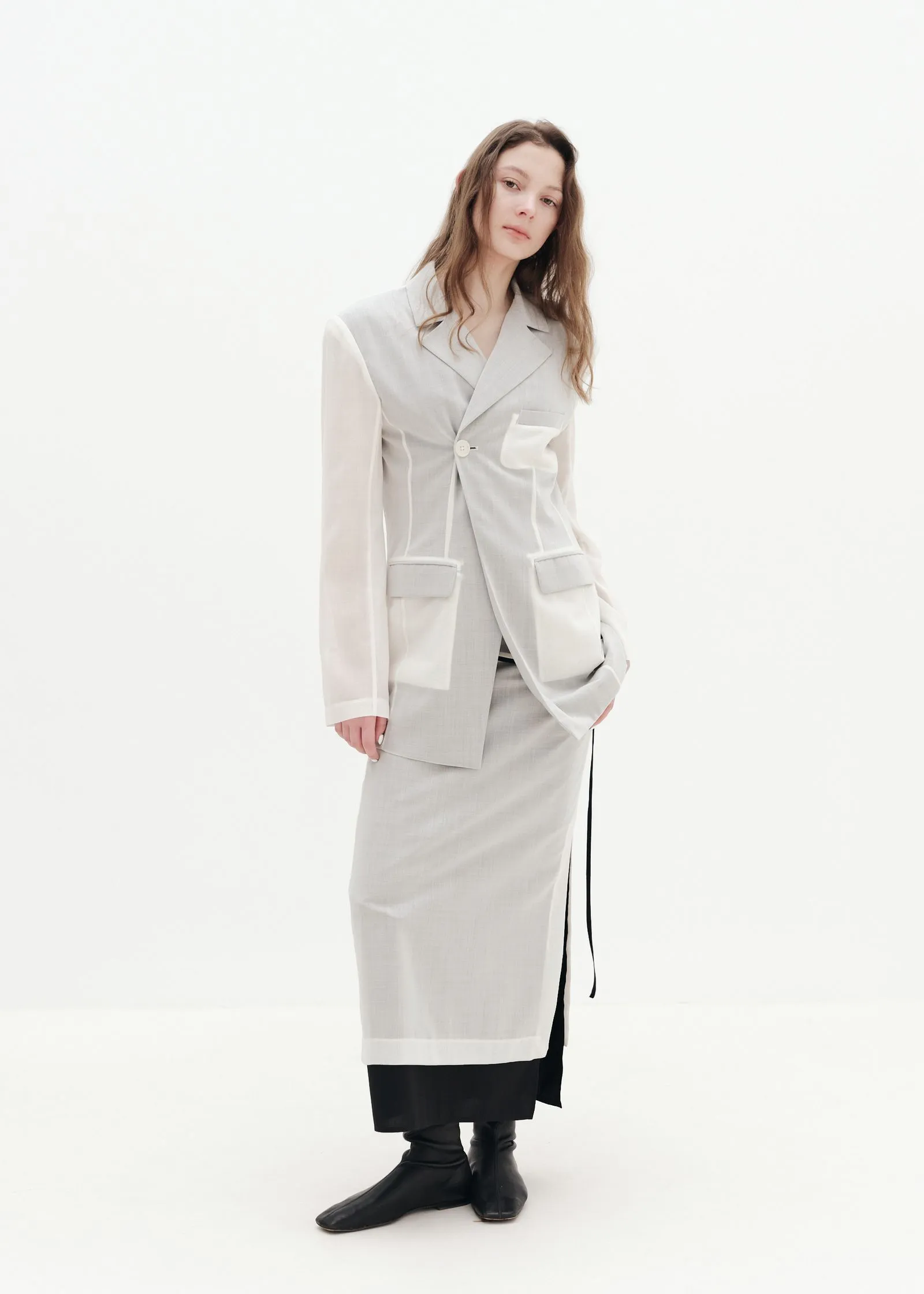 Person wearing a light gray blazer and matching skirt, standing against a white background.