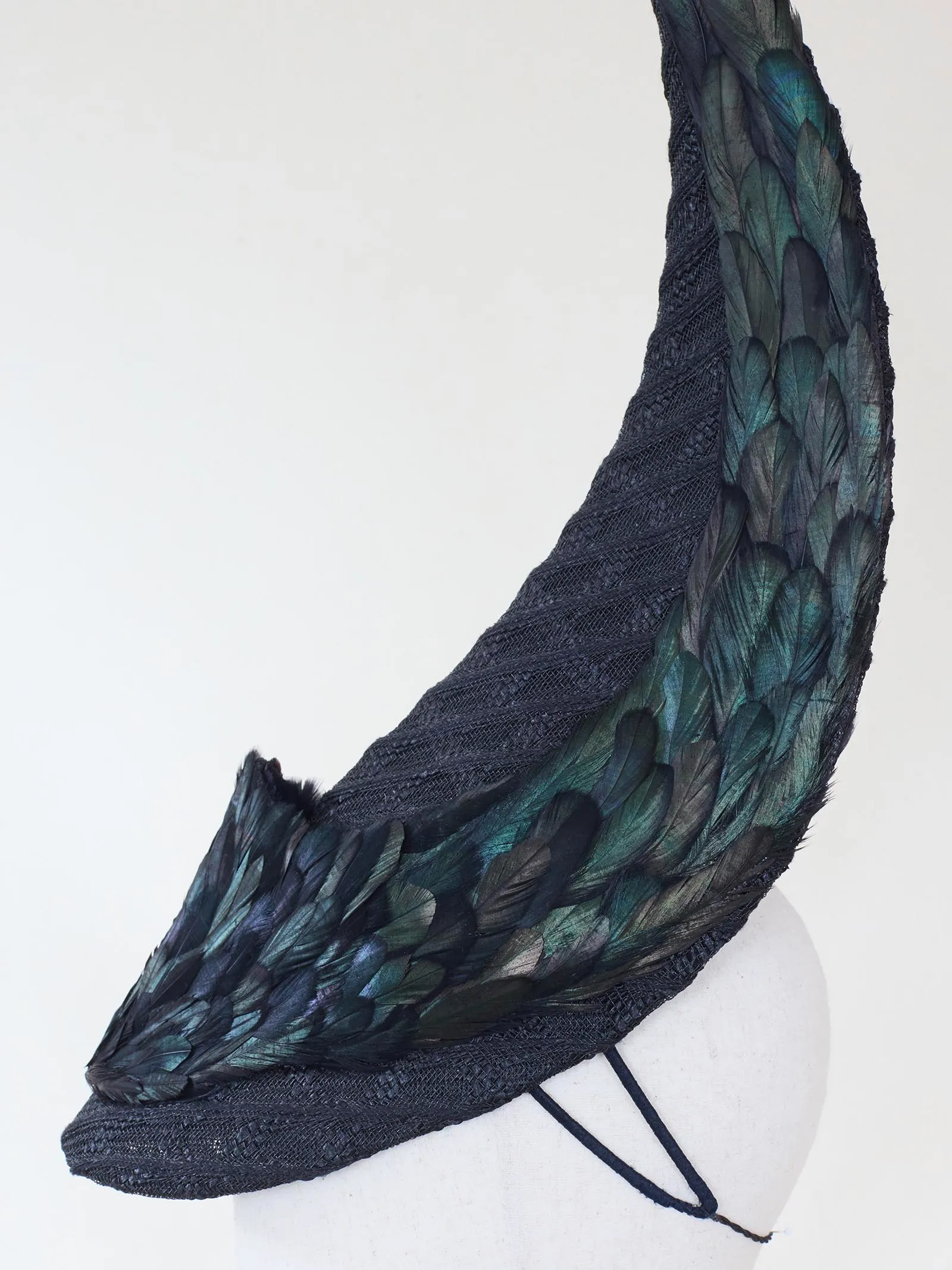 Dark, feathered scarf with iridescent teal-green feathers wrapped around a white mannequin bust.