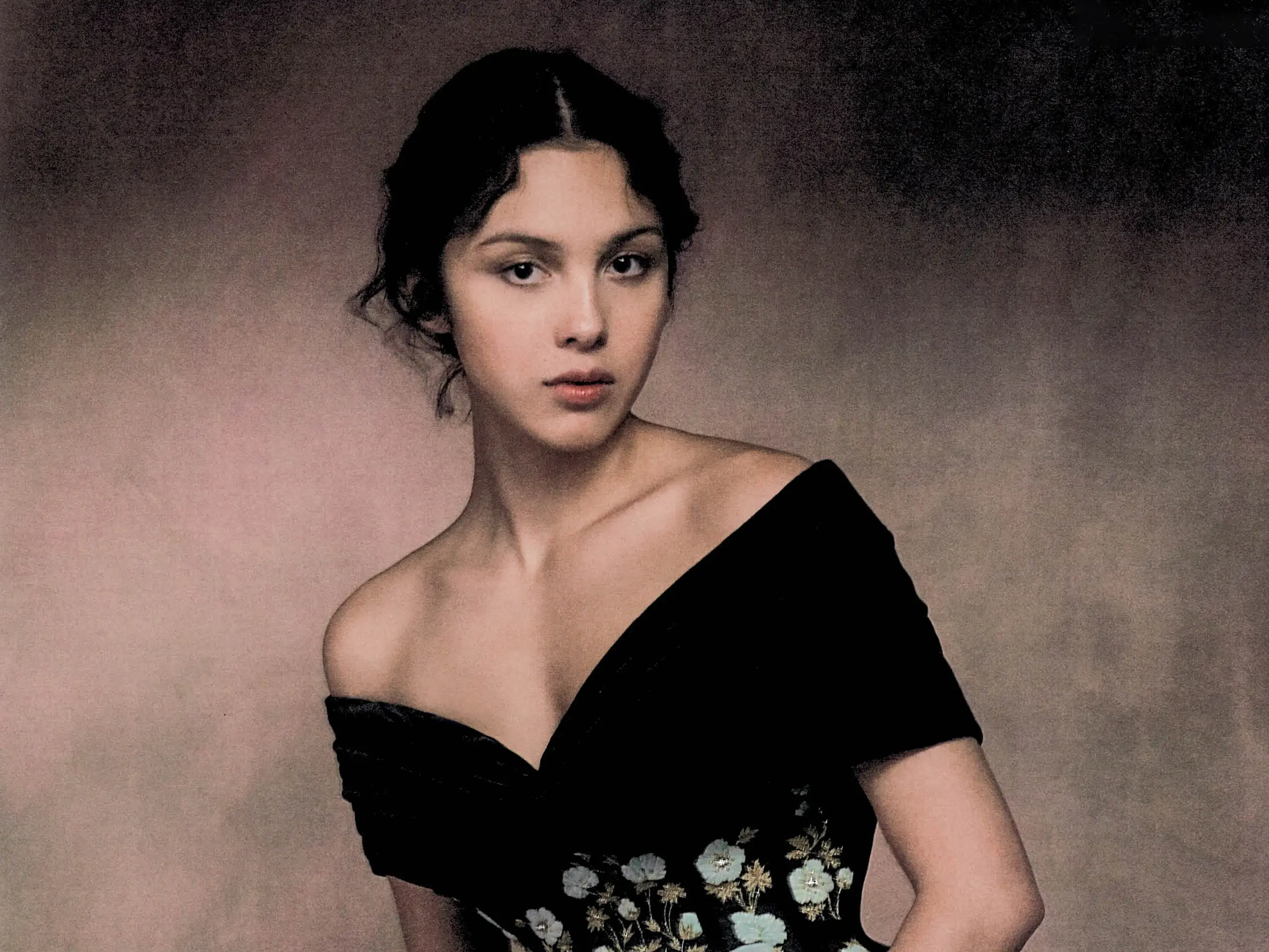 Portrait of a woman in a black off-shoulder dress with floral embroidery against a muted backdrop.