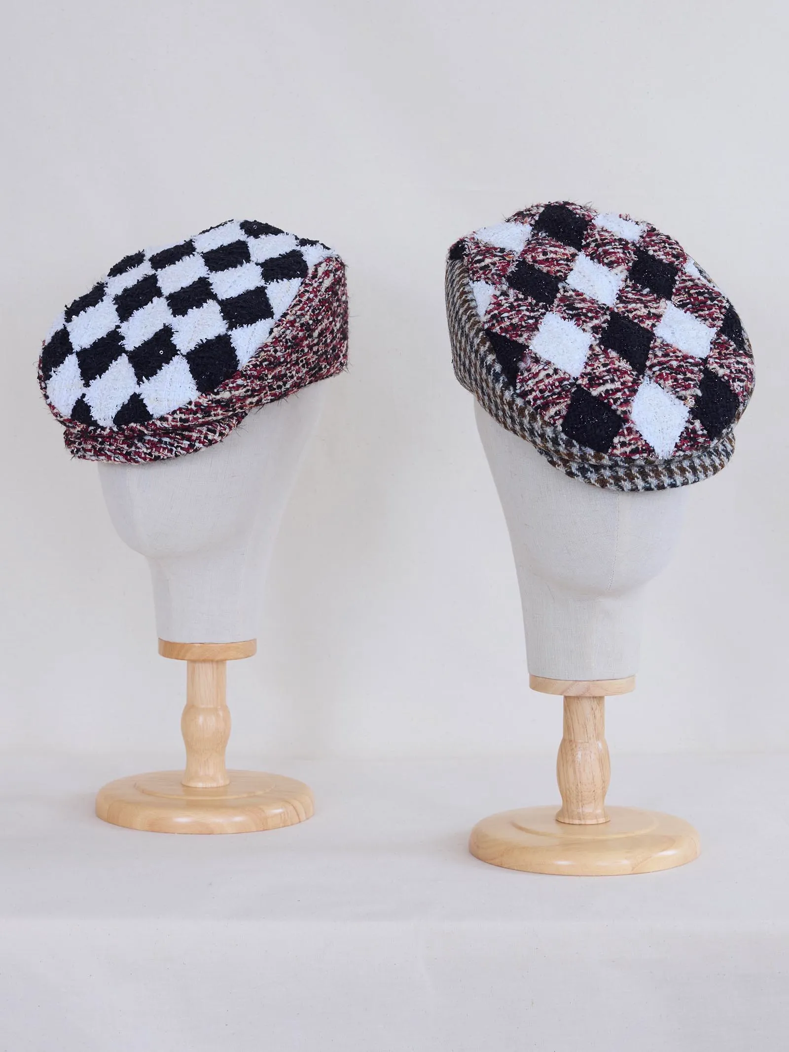 Two plaid wool caps displayed on white mannequin heads, one black-and-white checkered and the other burgundy-black-white checkered.