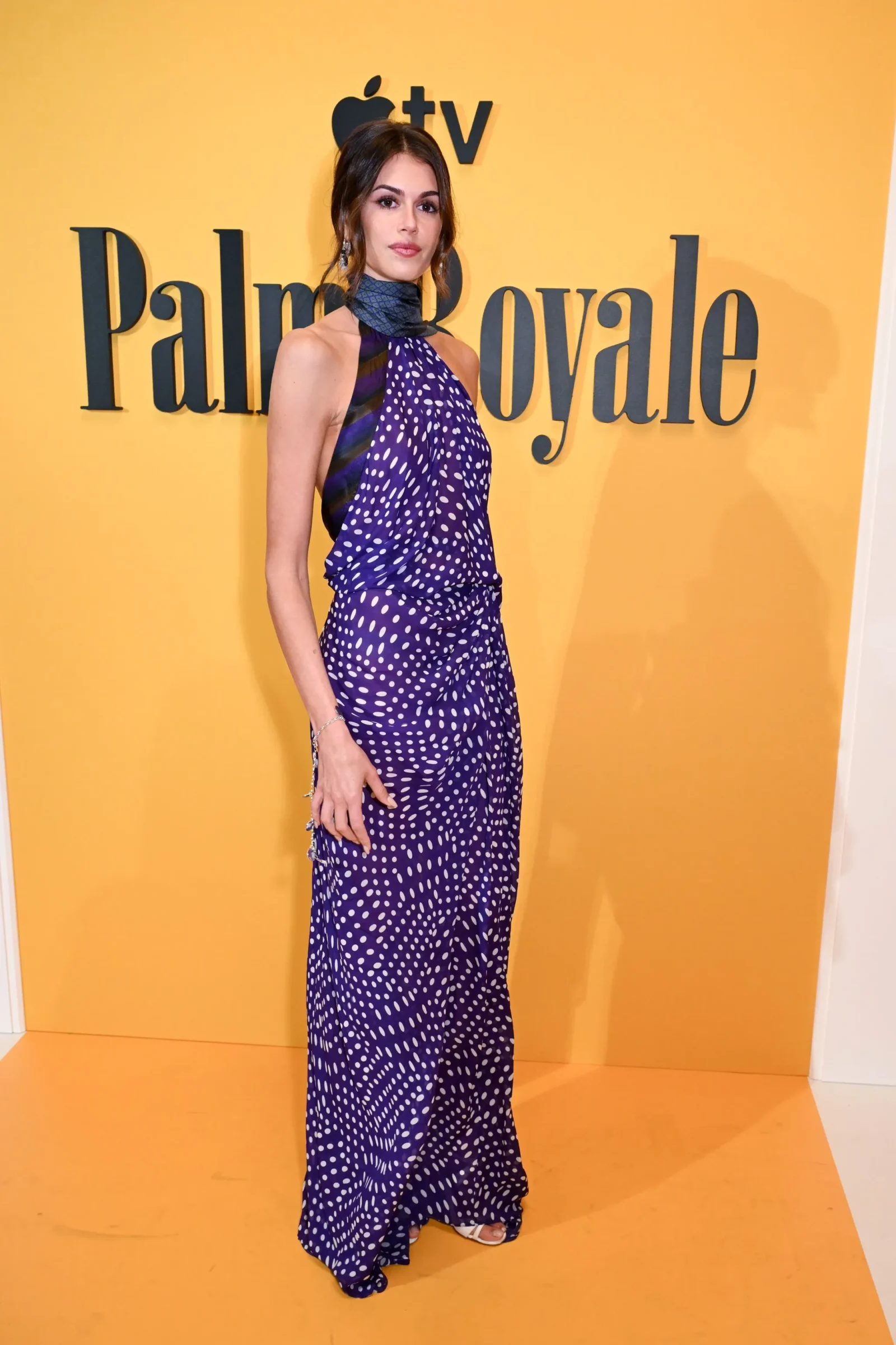 Woman in a purple polka-dot halter dress posing in front of a Palm Angels yellow backdrop.