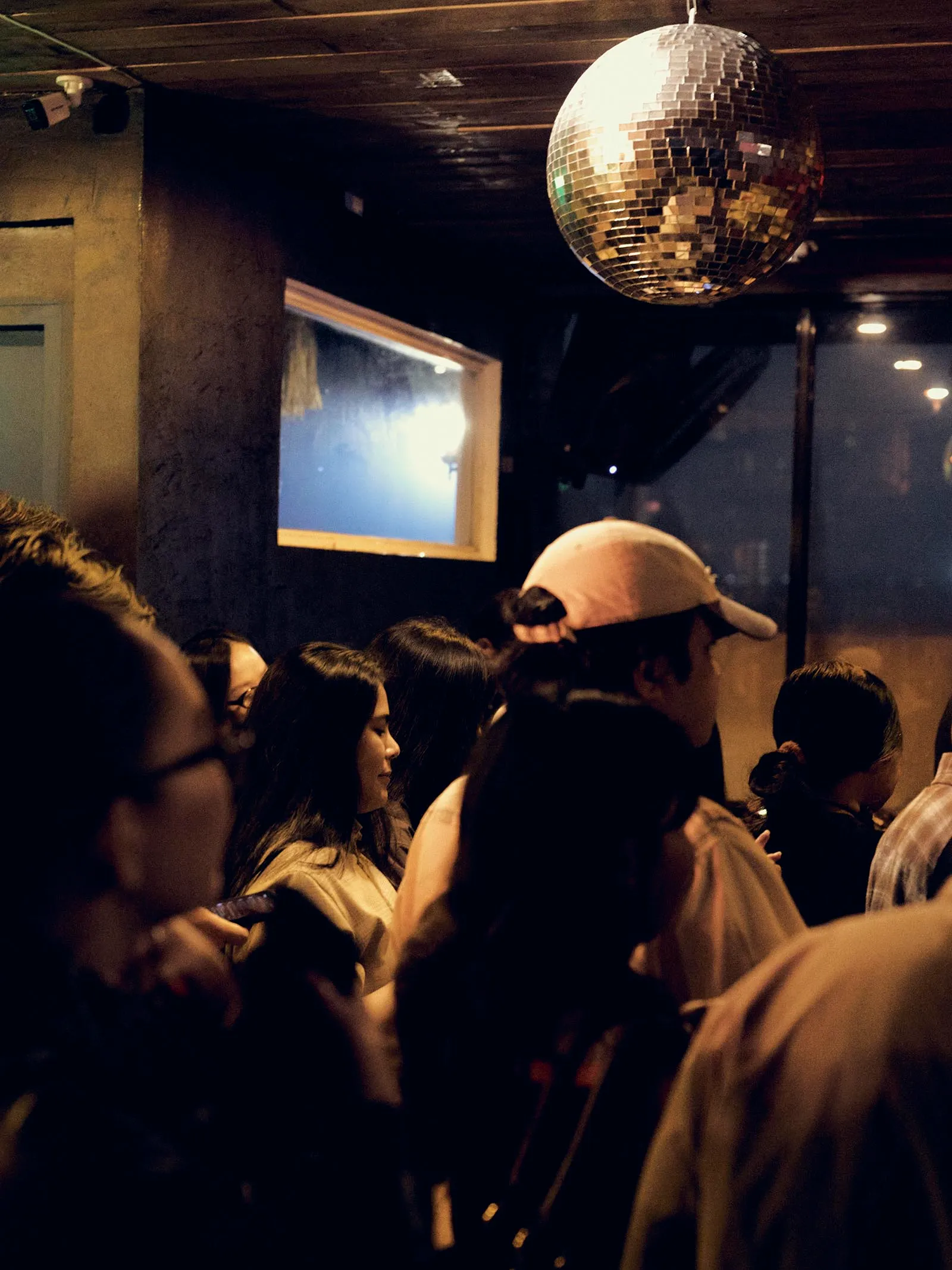 Crowd of people in a dimly lit club with a mirrored disco ball hanging from the ceiling.