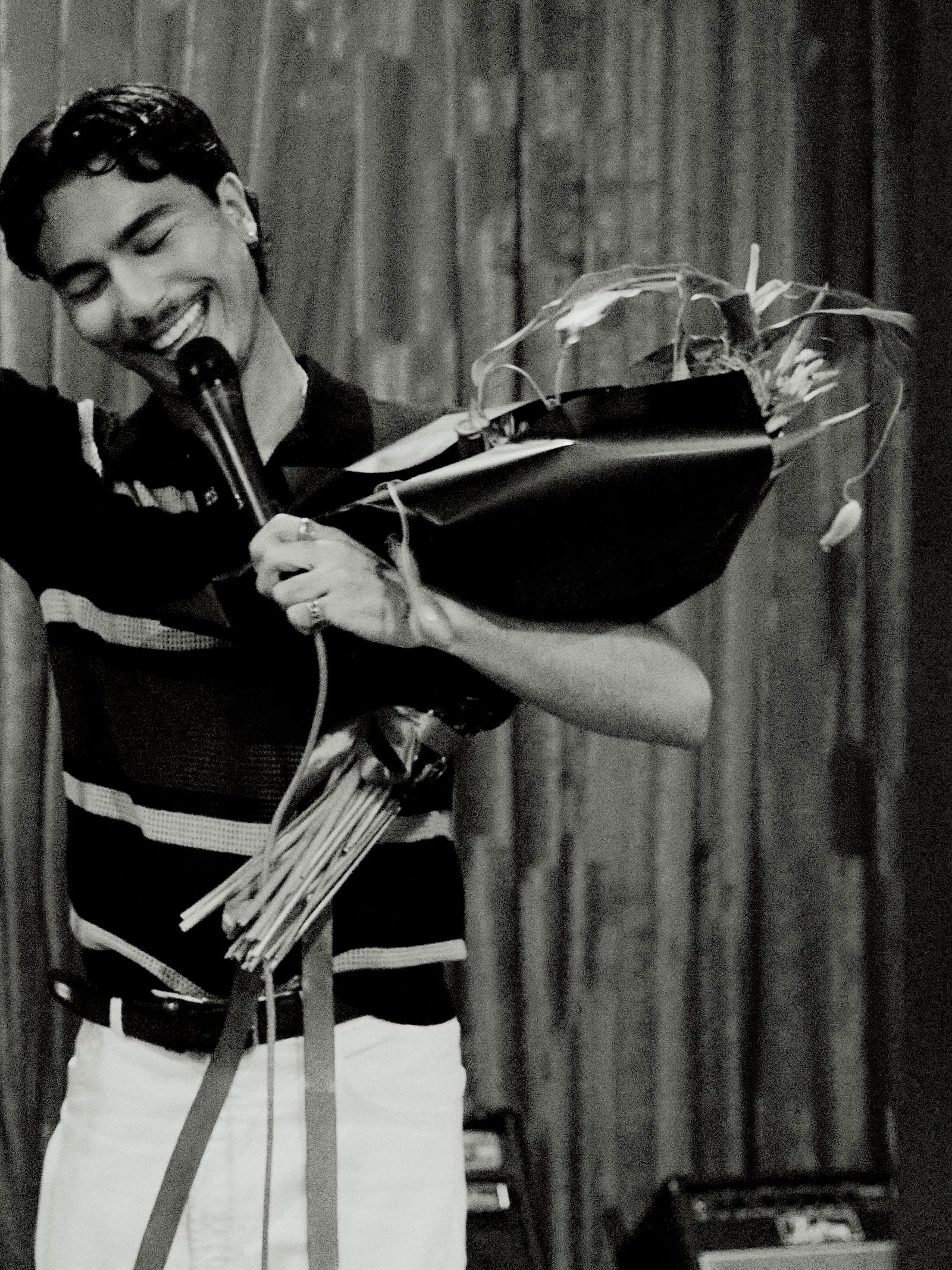 Male singer smiling into a microphone on stage, holding a large bouquet of flowers wrapped in paper; black-and-white photo