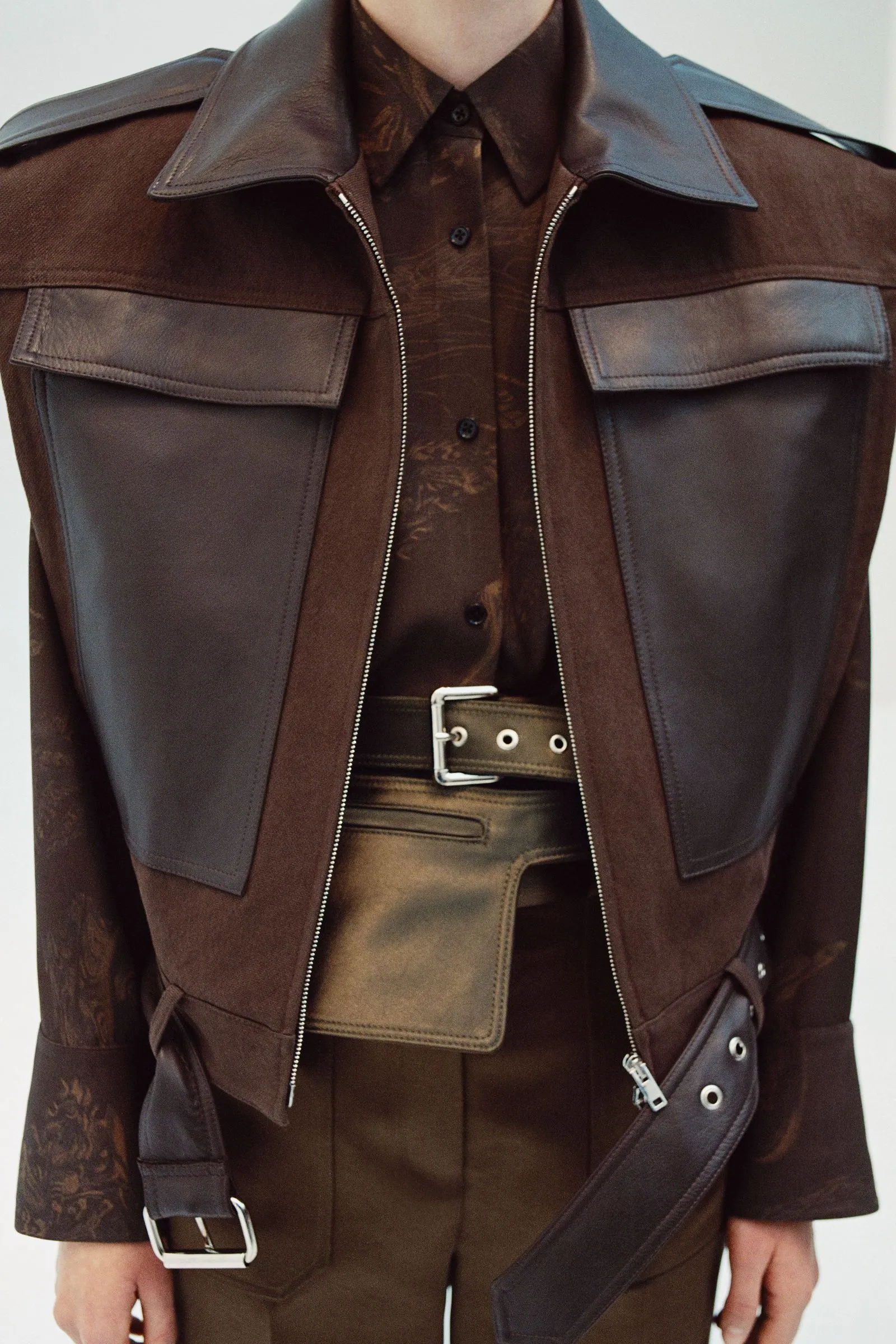 Close-up of a person wearing a brown leather jacket with front pockets and a belt