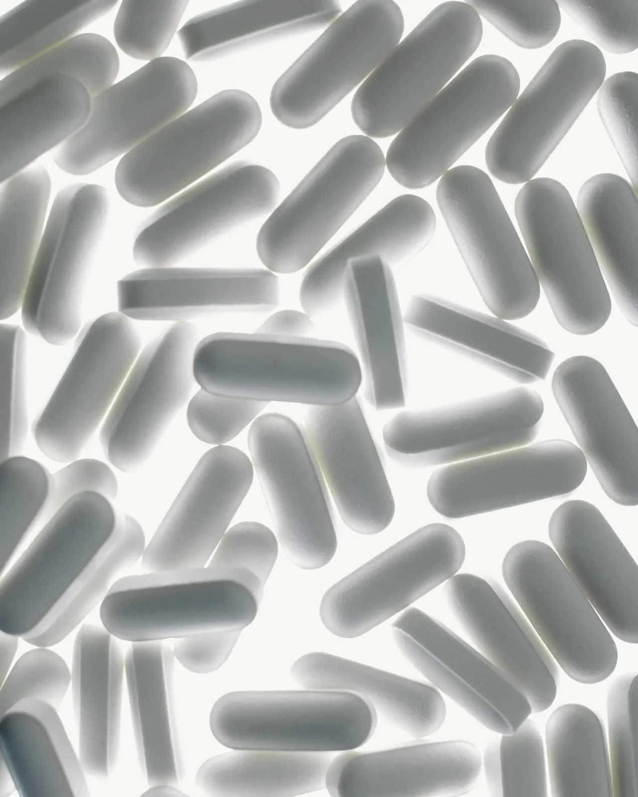 Scattered white capsule pills on a bright white background