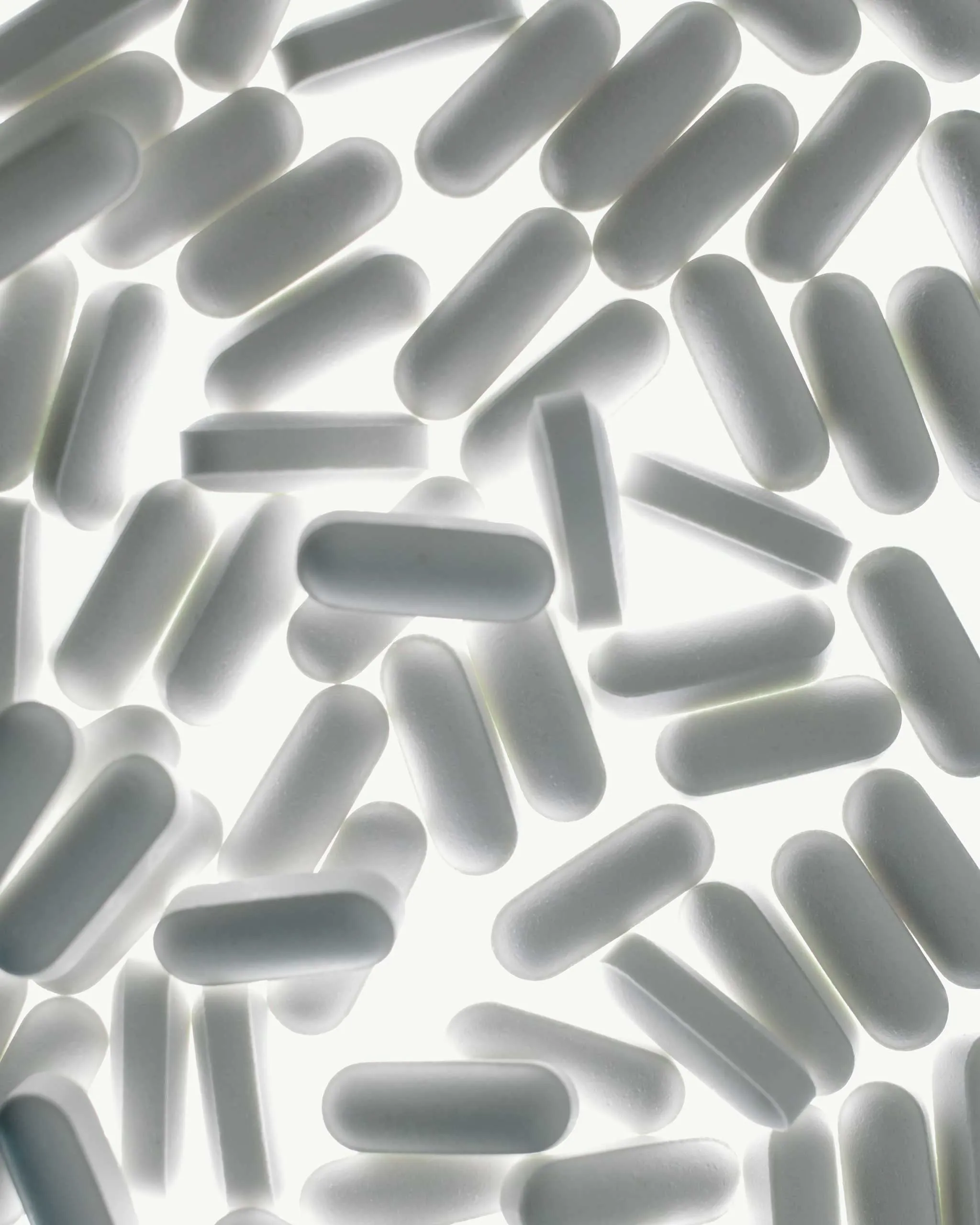 Close-up of many white capsule pills scattered on a bright surface.
