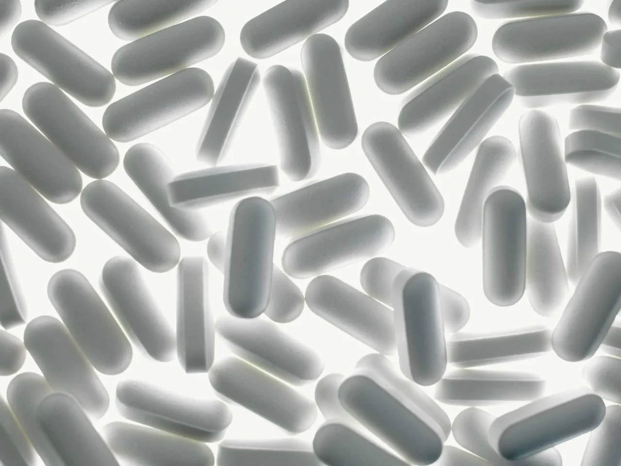 Scattered white capsule pills on a bright white background