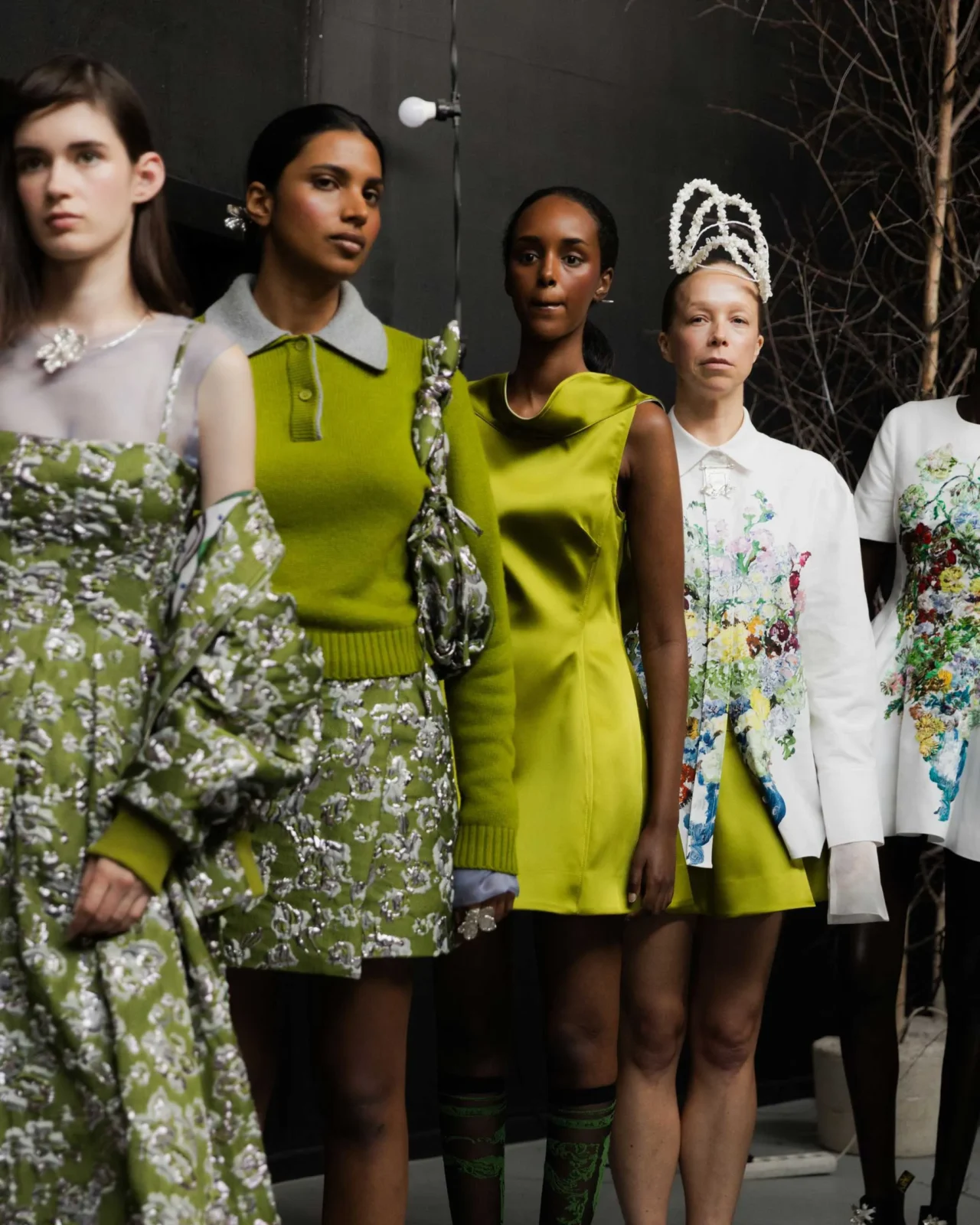 Group of diverse young people posing on a stage in colorful, eclectic outfits and accessories against a dark backdrop.