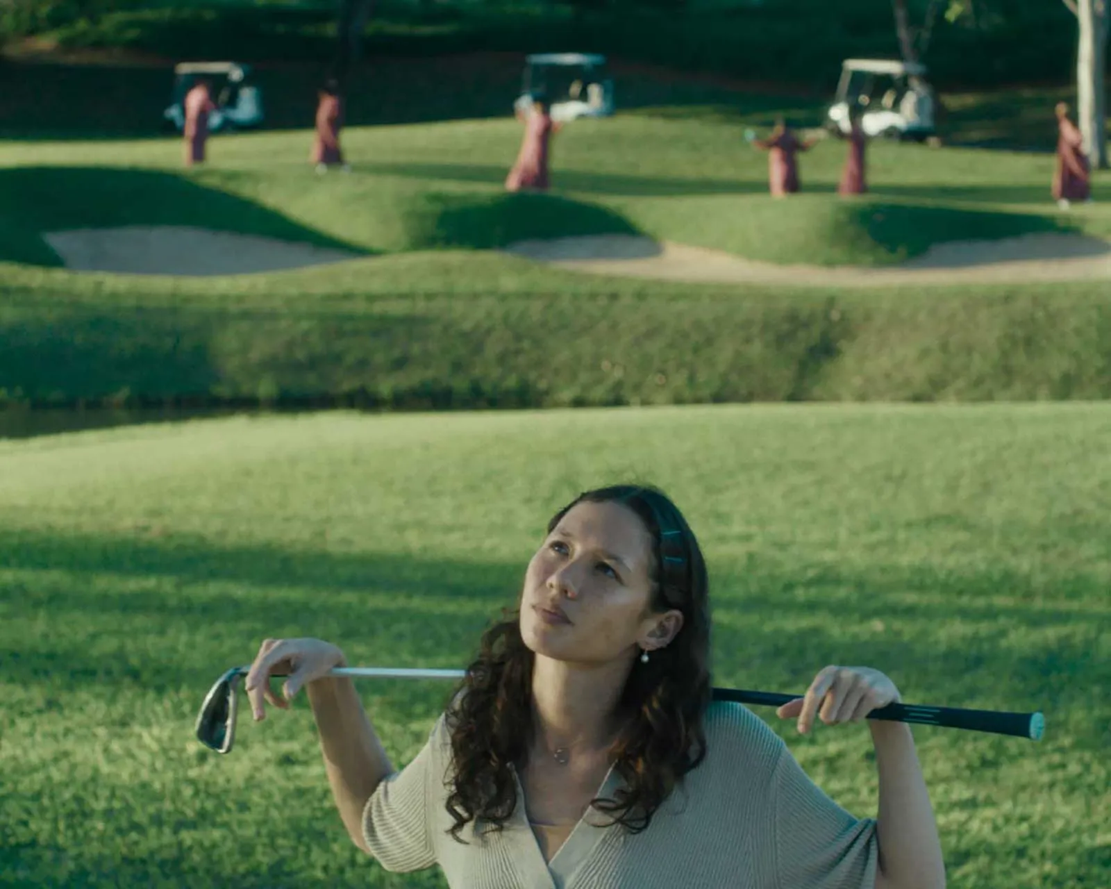 Woman in a park holding a long rod behind her neck while looking upward, with green rolling hills in the background.