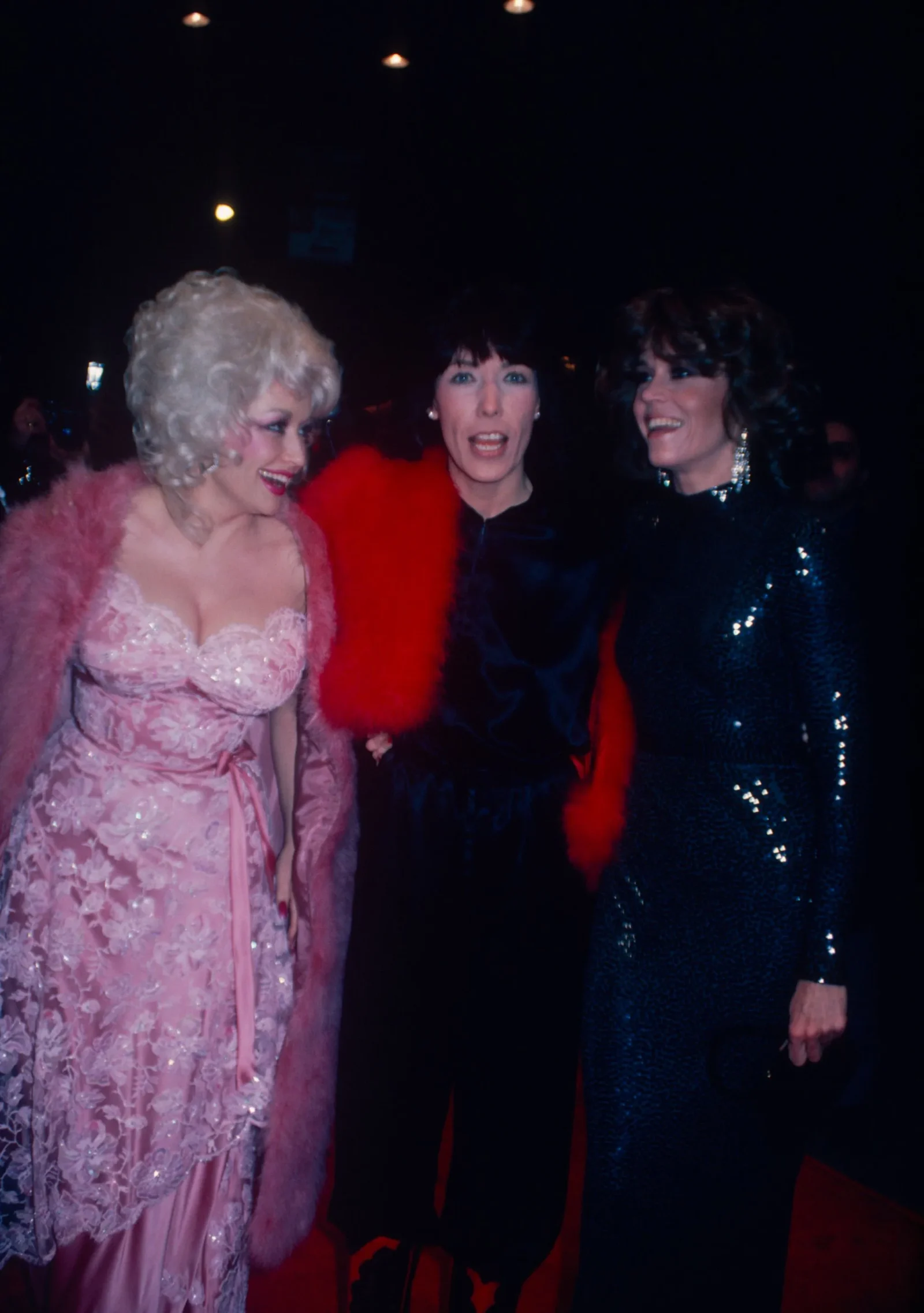 Three drag queens in glamorous gowns posing together at a dim party venue.