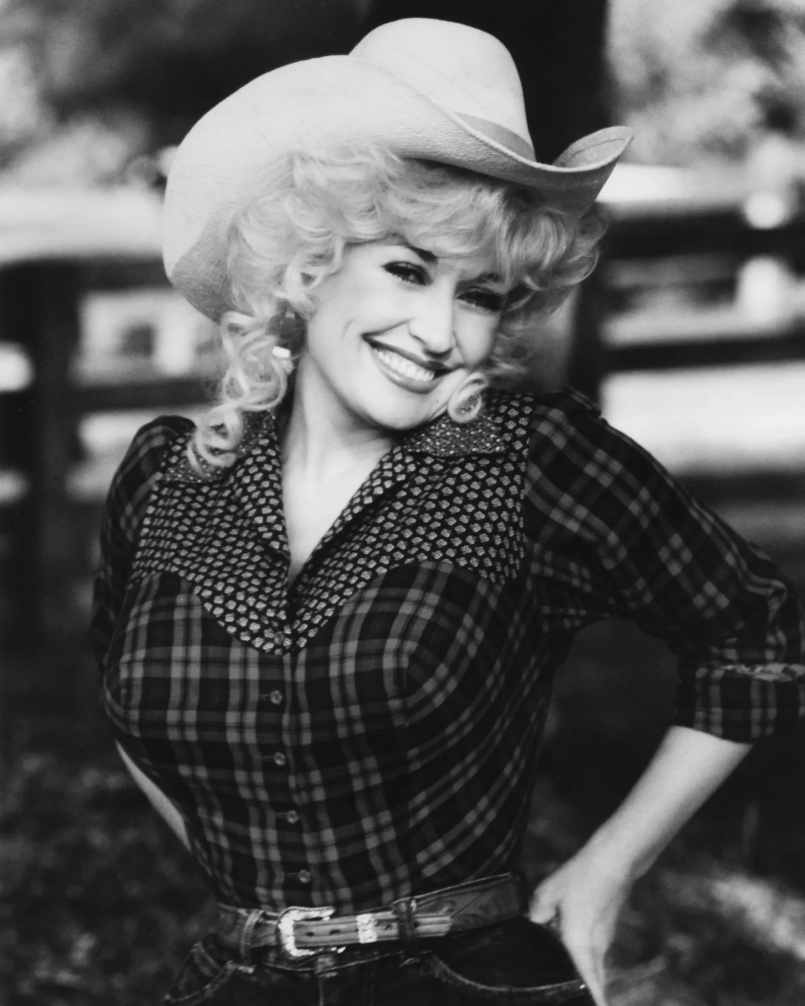 Smiling woman wearing a wide-brimmed hat and plaid shirt outdoors.