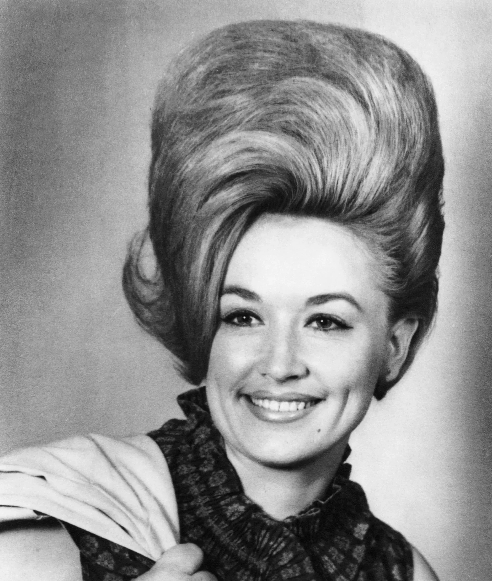 Black-and-white portrait of a smiling woman with a large retro bouffant hairstyle in a vintage vibe.