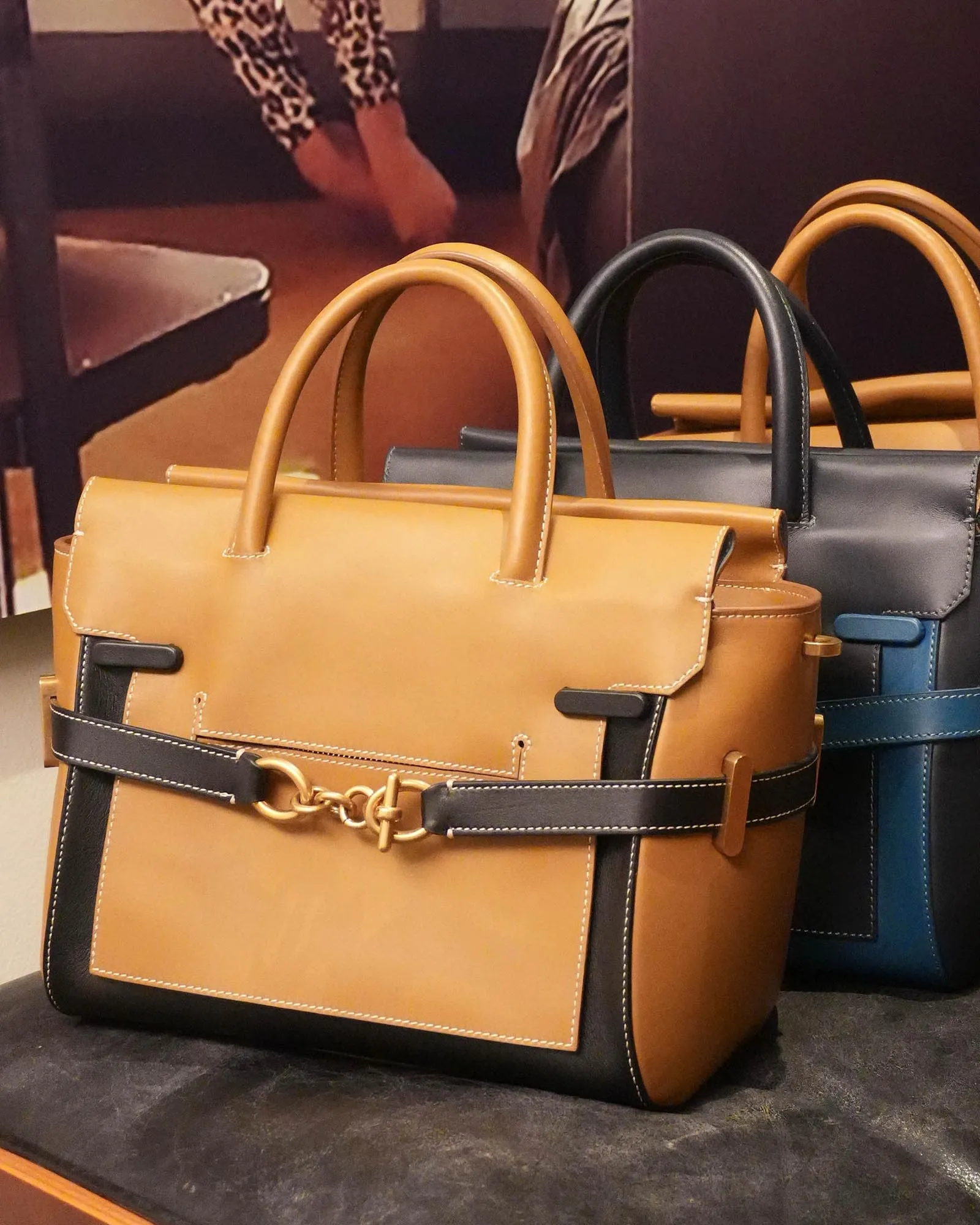 Stacked tan and black leather handbags with top handles on display