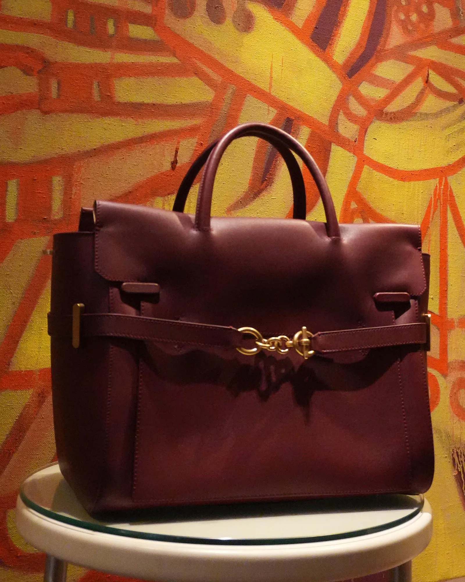 Brown leather handbag with gold chain clasp resting on a chair, set against a bright orange graffiti wall behind.