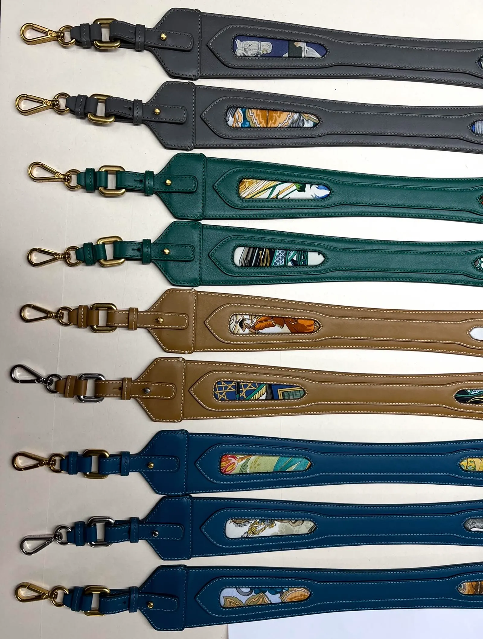 Row of colorful leather bag straps with brass hardware and decorative fabric insets, laid out side by side.