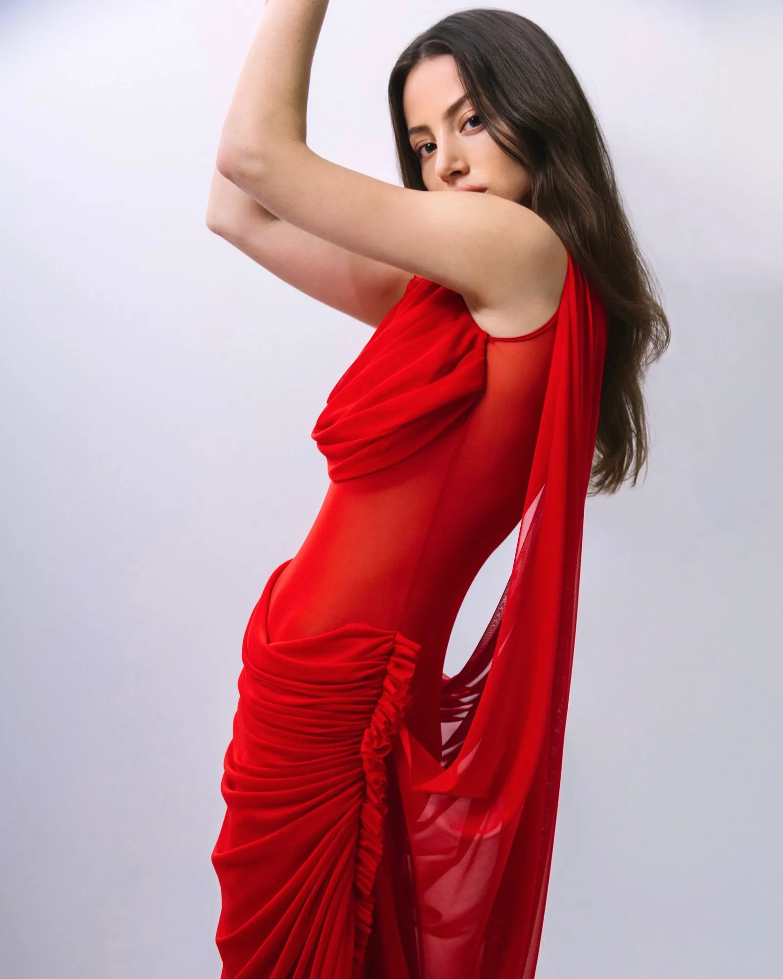 Woman in a red dress raises her arm in a dynamic studio pose, facing left.