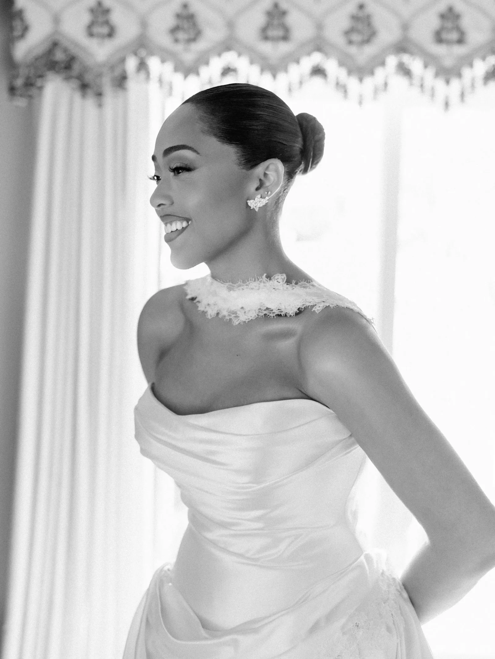 Bride in a strapless wedding gown with lace neckline, smiling in profile against a light background.