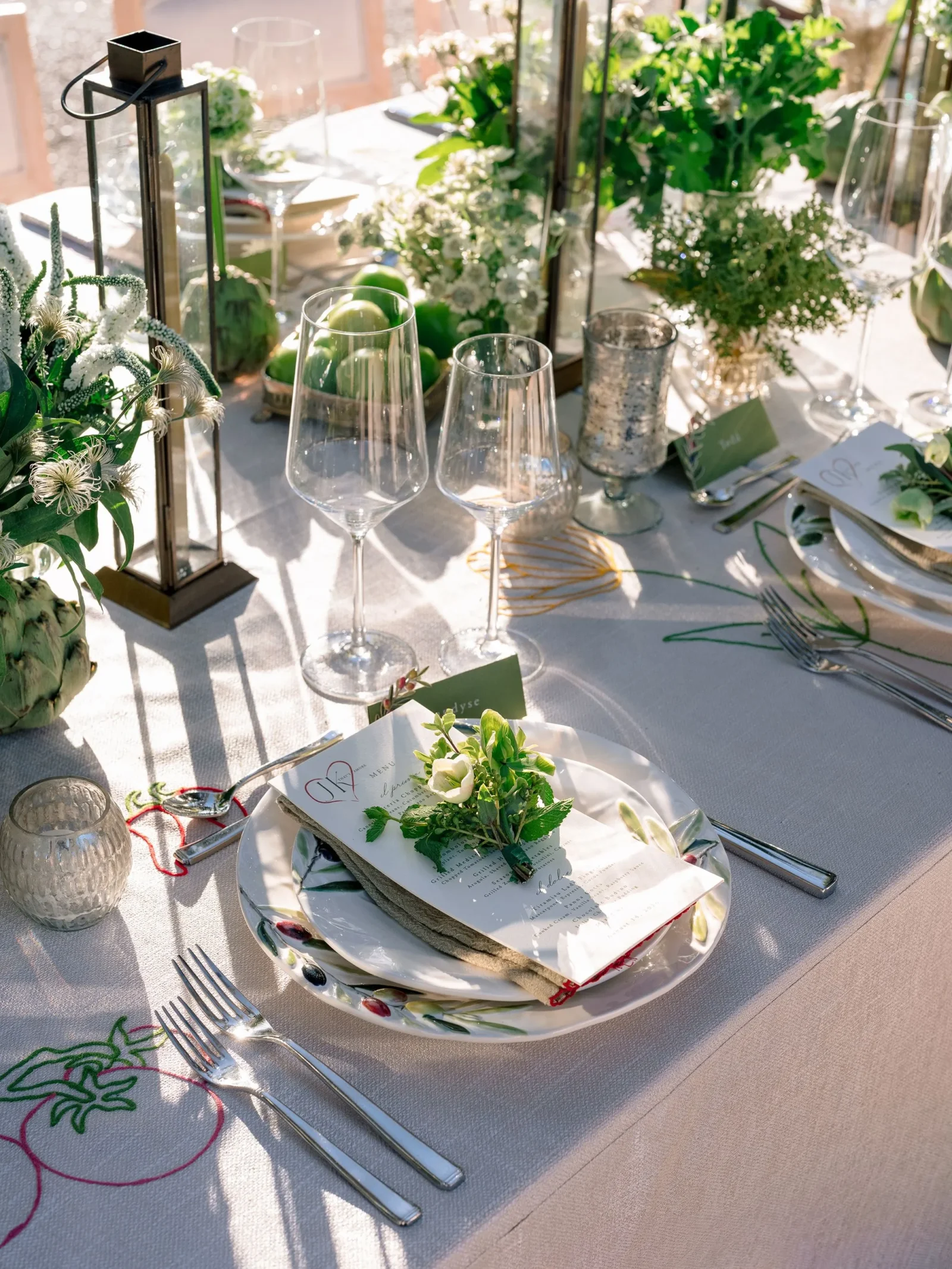 Elegant table setting with stemware, plates, and floral centerpiece for a formal meal, featuring a menu card and greenery.