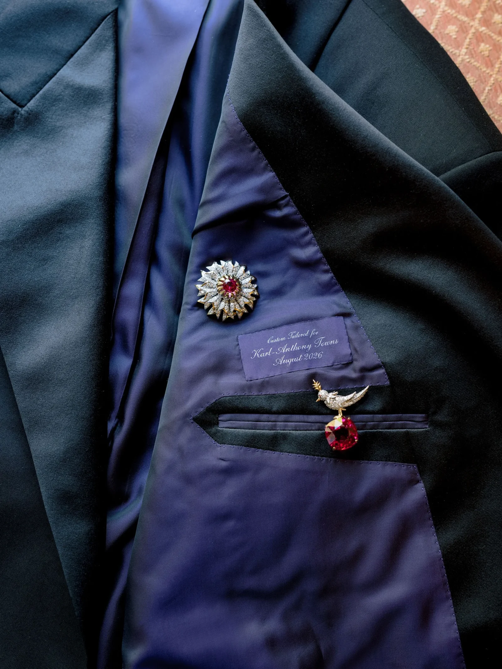 Close-up of a dark blue suit lining with a jeweled starburst brooch and red centerpiece on the lapel pin