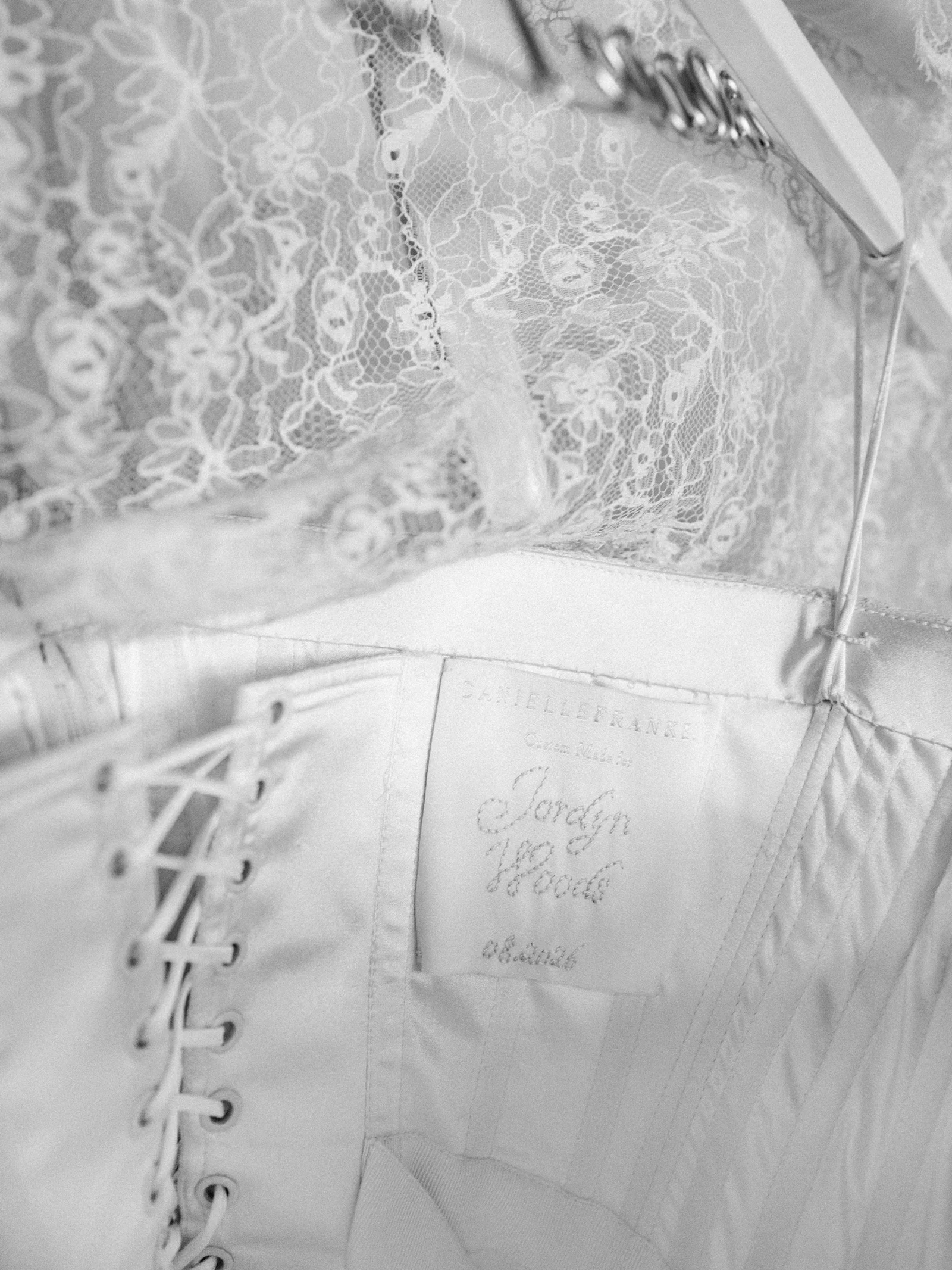 Close-up of delicate white lace lingerie (corset/bustier) with hooks, hanging on a hanger.