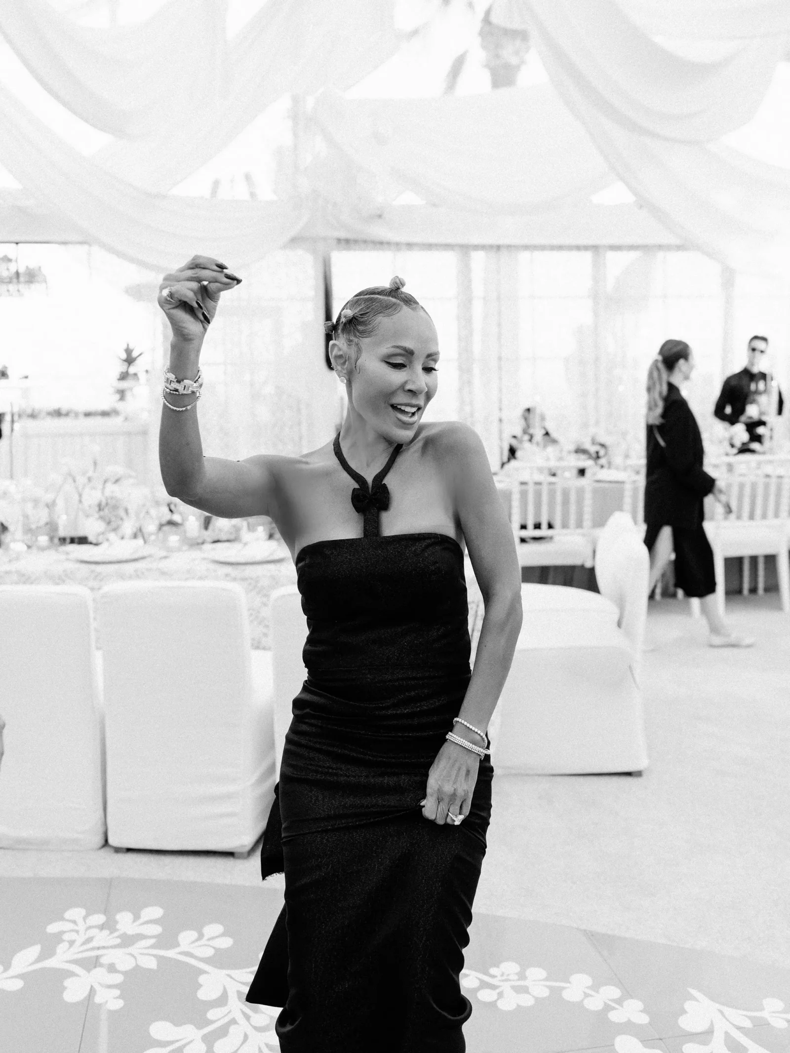 Woman in a black strapless dress dancing, smiling, with her right arm raised at a formal event.