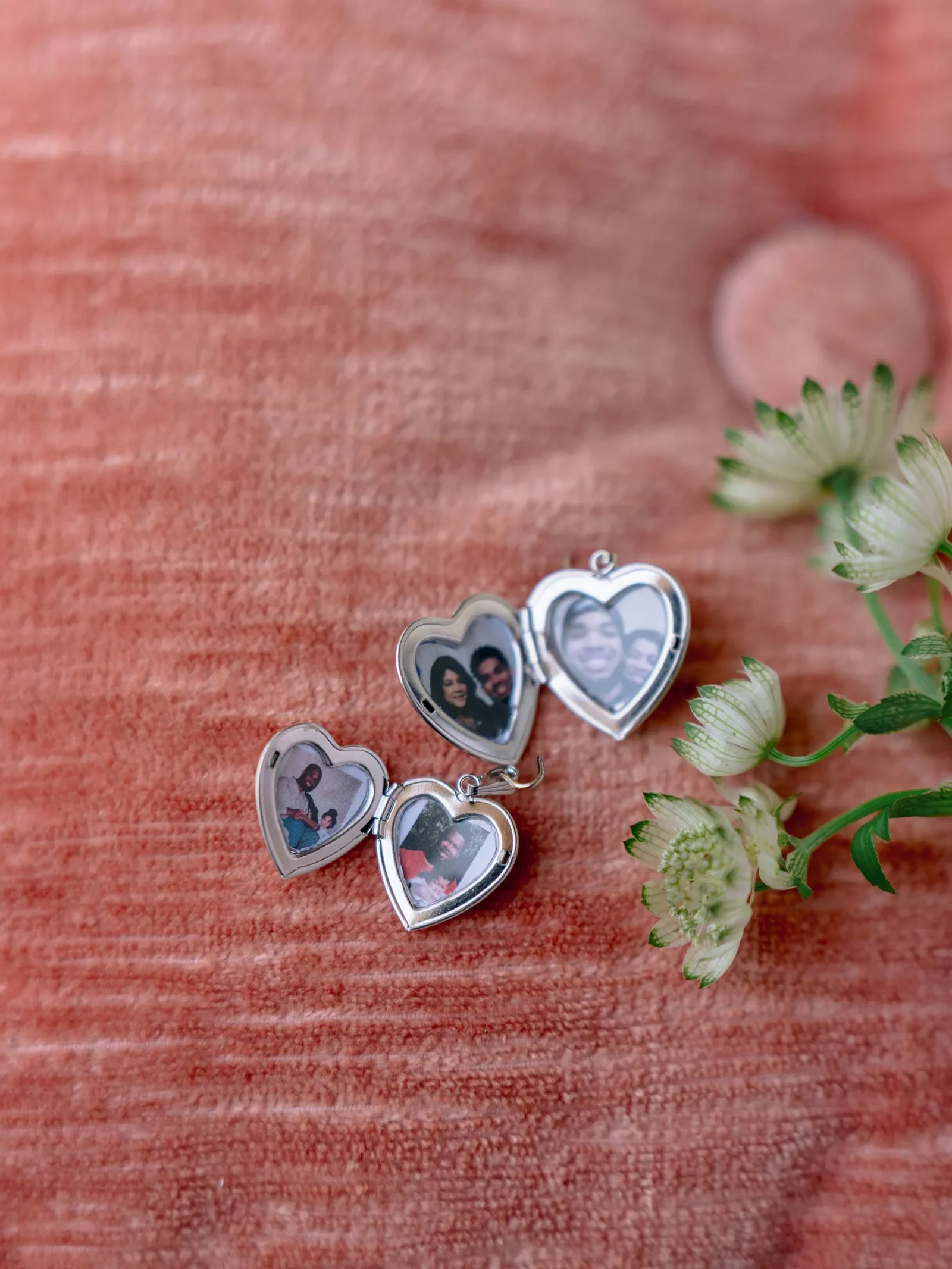 Heart-shaped locket bracelet opened to reveal small photos on a red textured surface with white flowers nearby.