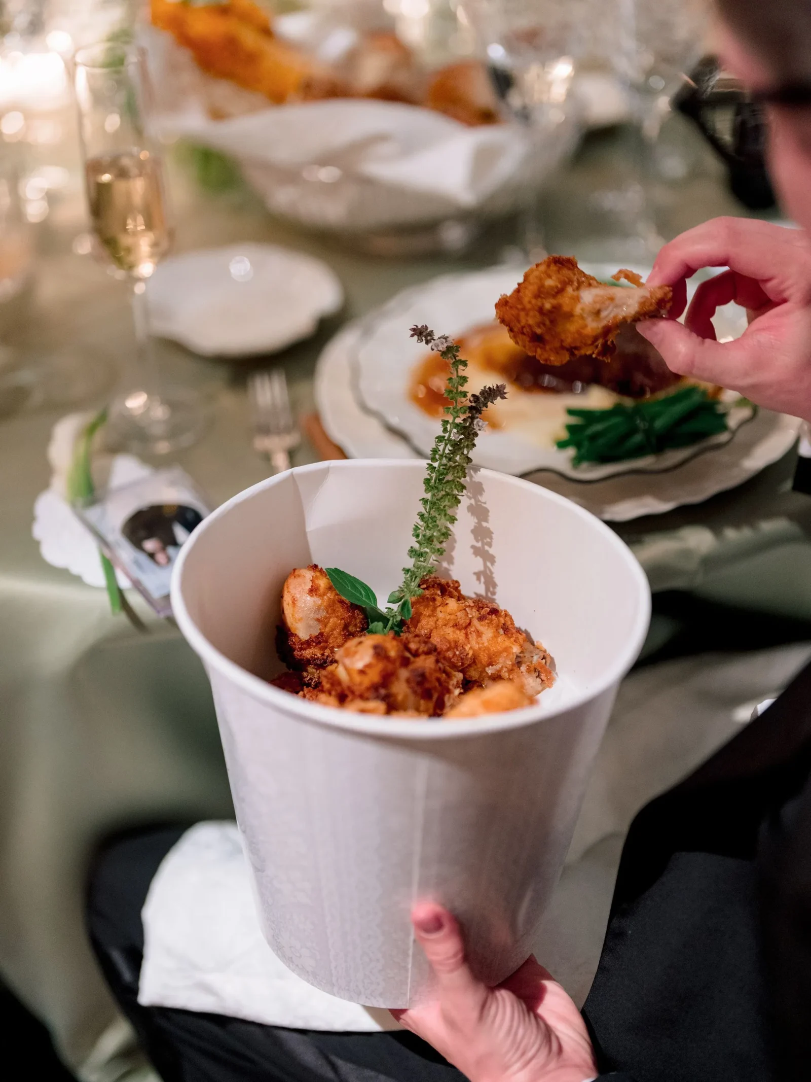Fried chicken bites served in a white cone, being picked up by a hand at a dining table.