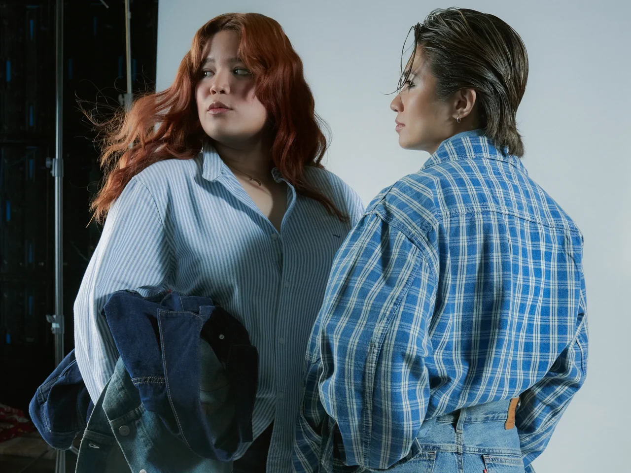 Two people in blue striped shirts pose against a neutral backdrop; woman with red hair looks left while man faces away.