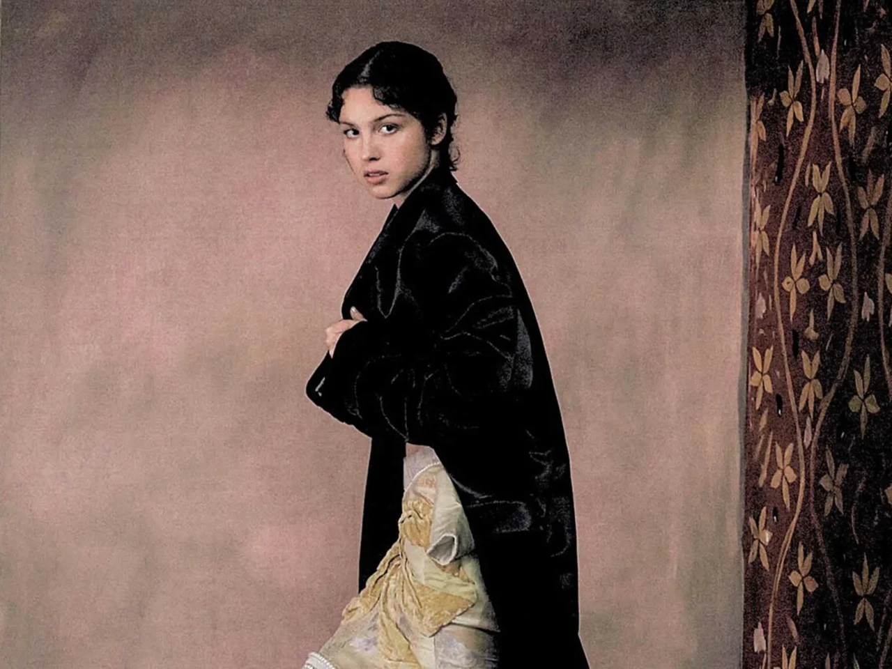 Portrait of a woman wearing a white robe with a black rectangular panel, standing against a pale pink backdrop.
