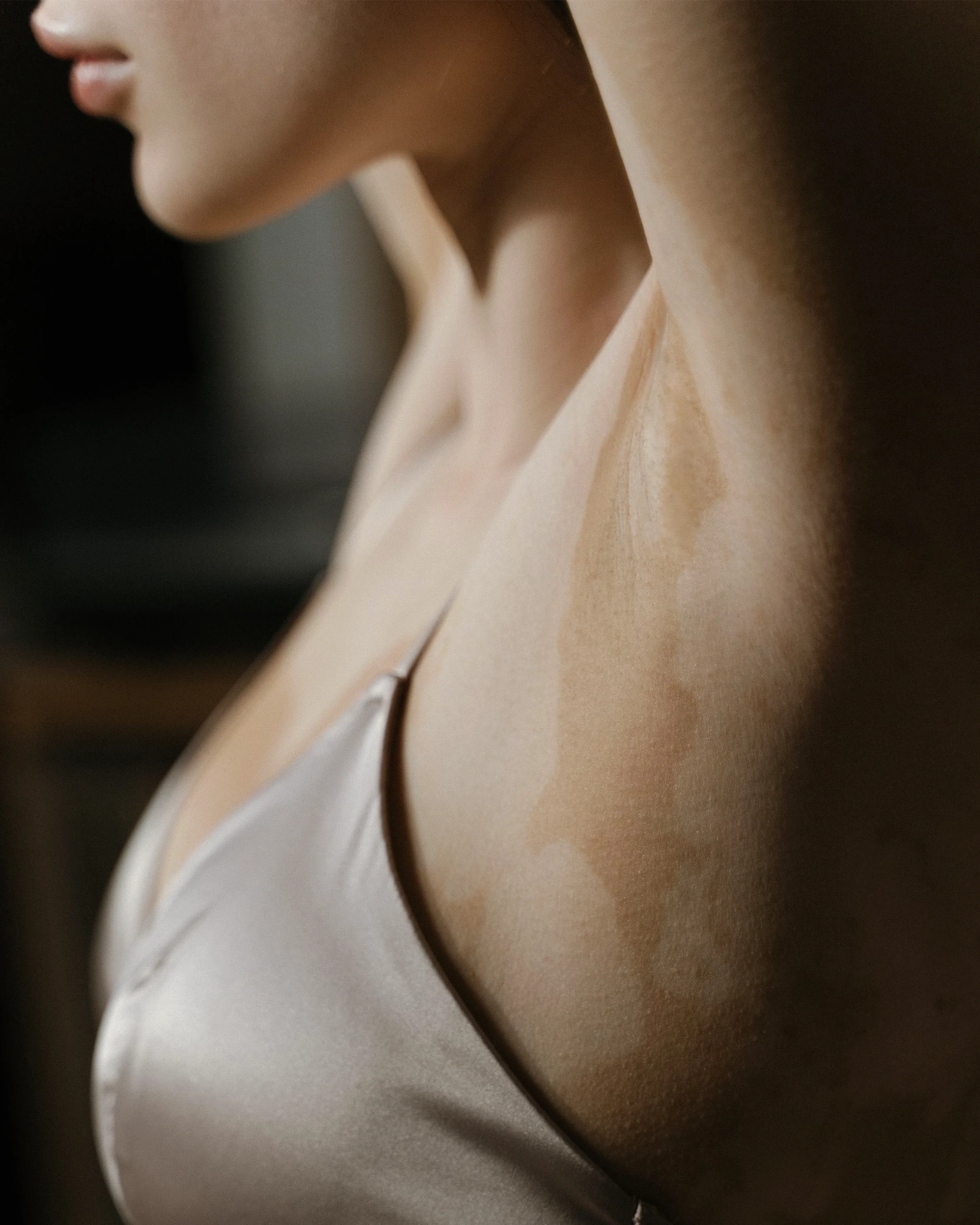 Close-up of a woman's neck and shoulder in a white sleeveless top, viewed from the side.