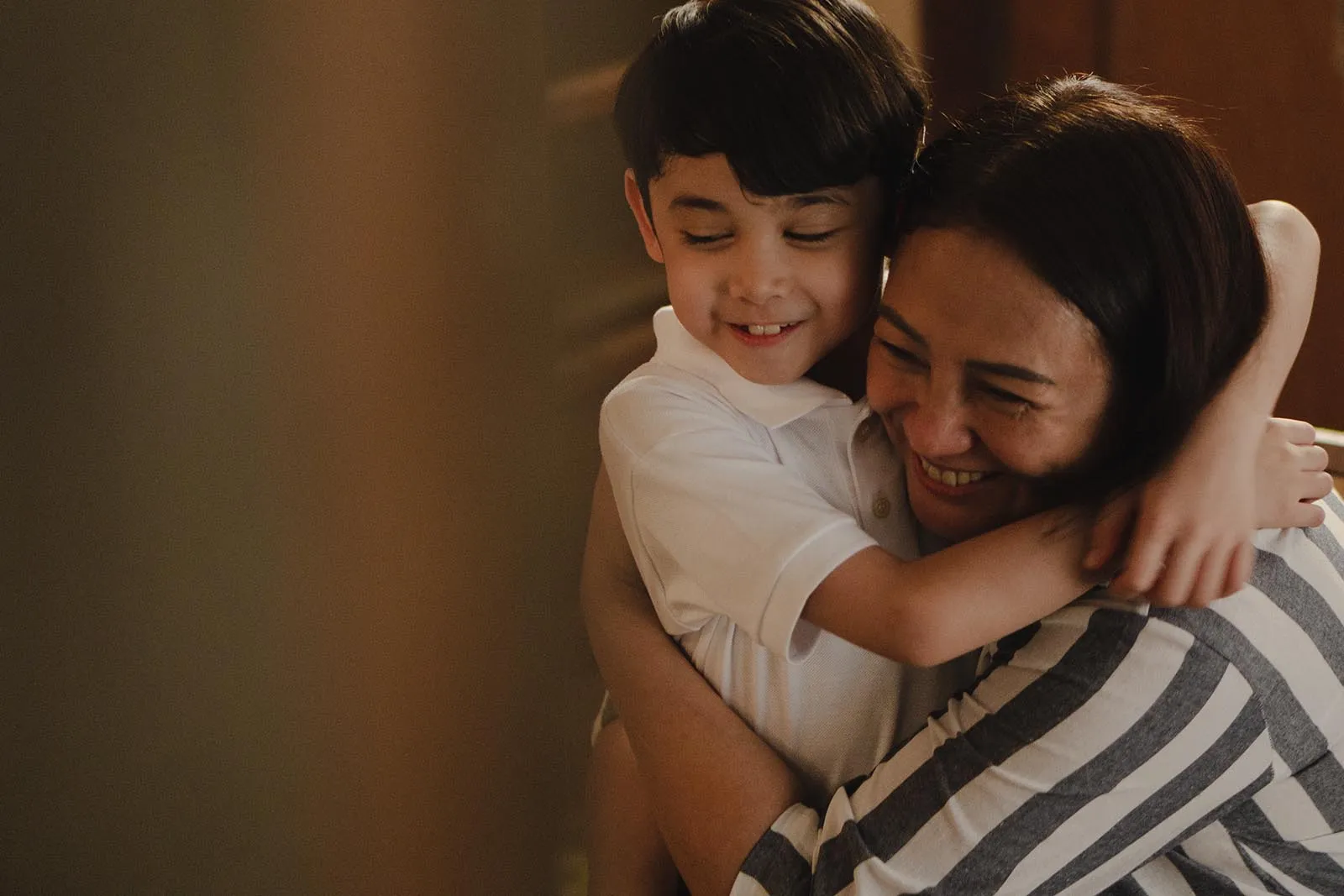 Boy hugging a smiling woman, likely his mother, in a warm embrace.