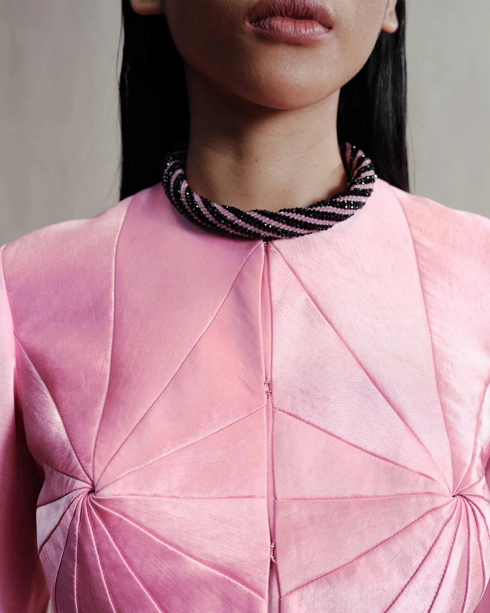 Close-up of a neck and lower face with a pink braided beaded choker over a pink garment.