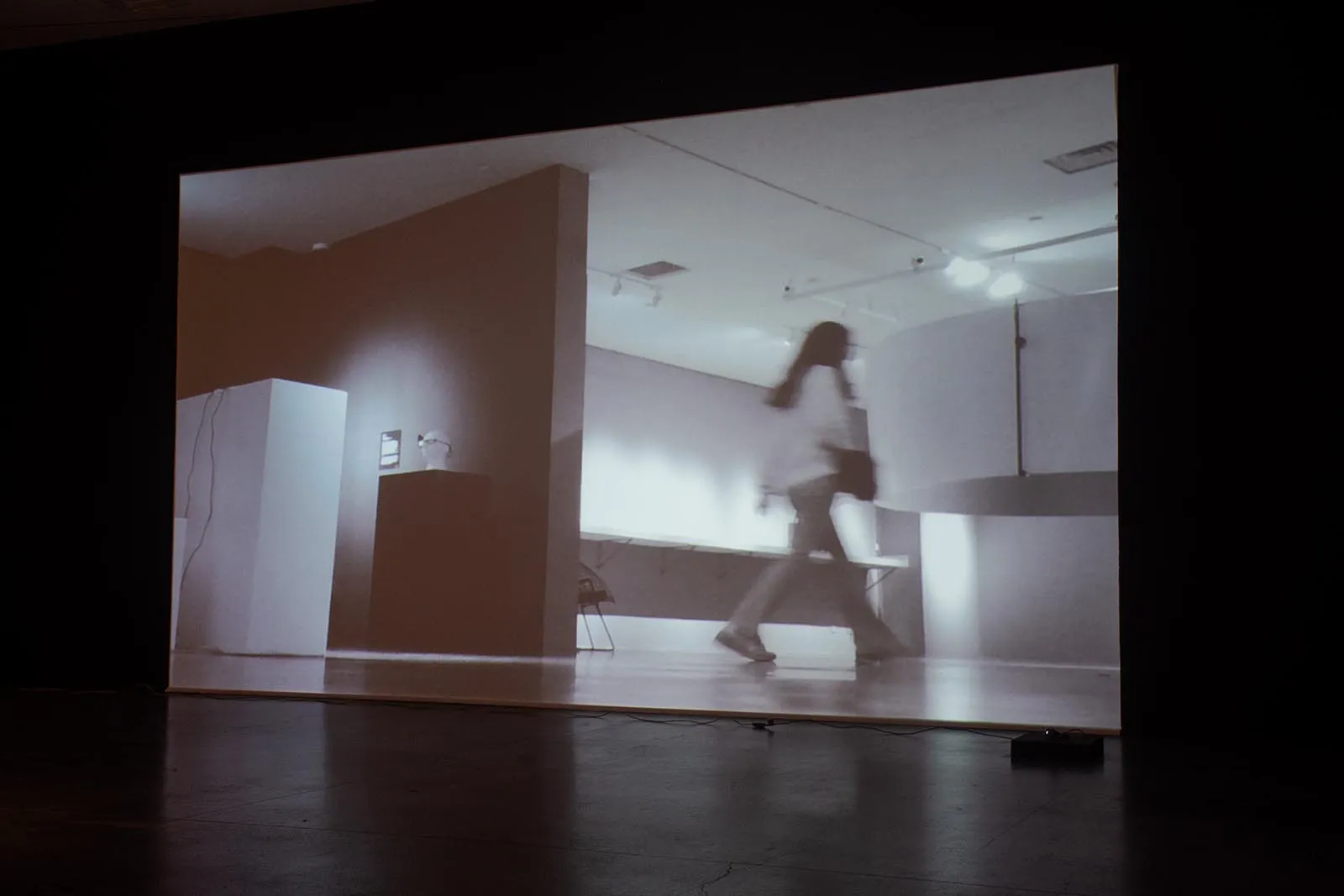 Monochrome video projection of a person walking through a modern interior space.