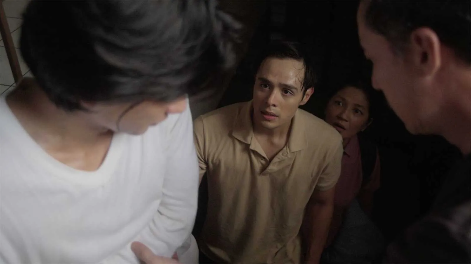 Tense moment in a crowded stairwell: a man in a beige polo shirt looks up at two others who flank him.