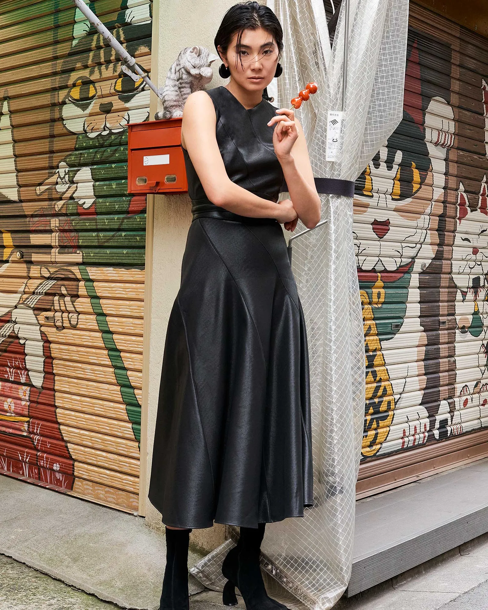 Woman in a black sleeveless dress poses with orange dango skewers in front of a graffiti mural.