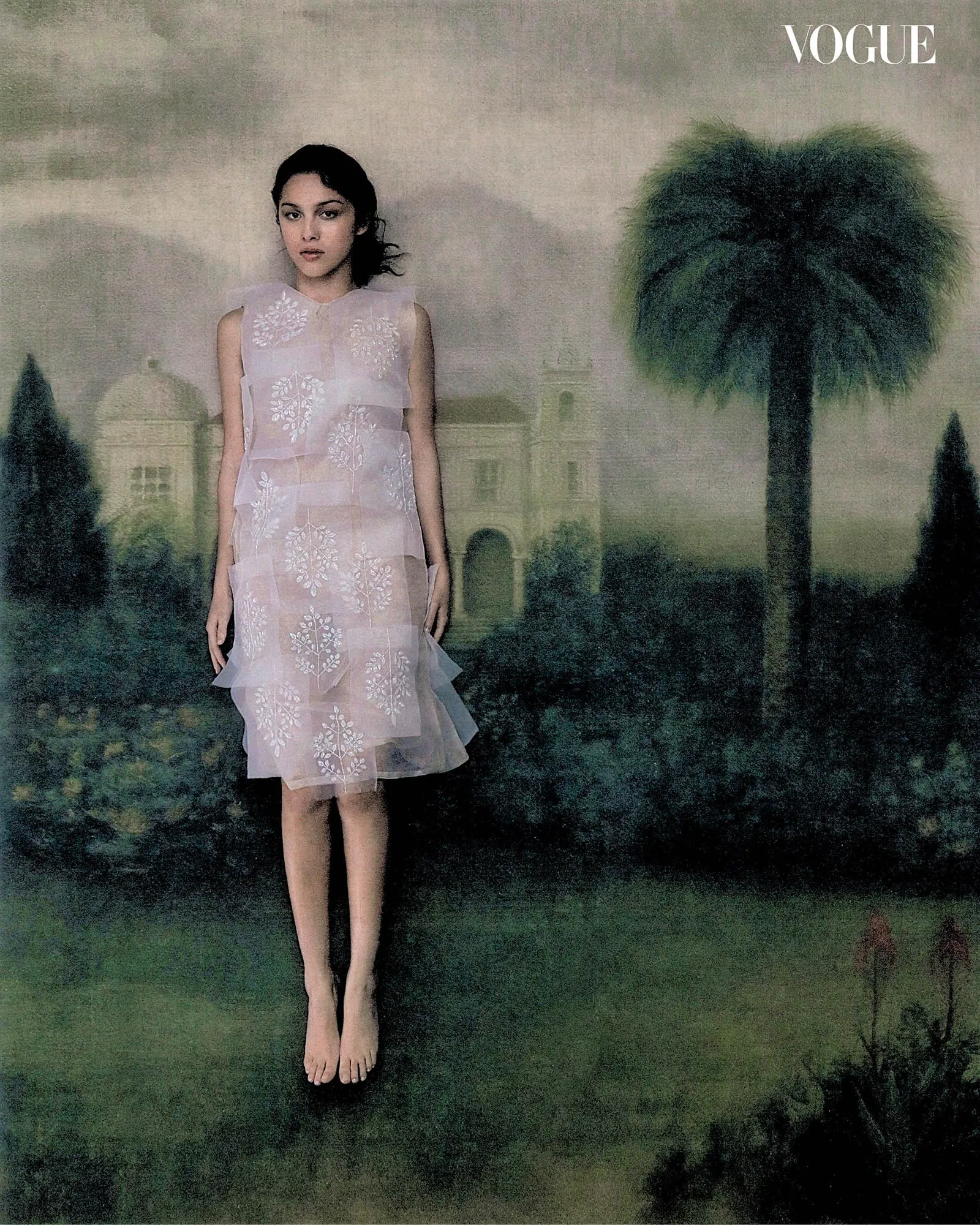 Vogue cover featuring a model in a pale pink embroidered dress standing barefoot outdoors with a palm tree in the background.