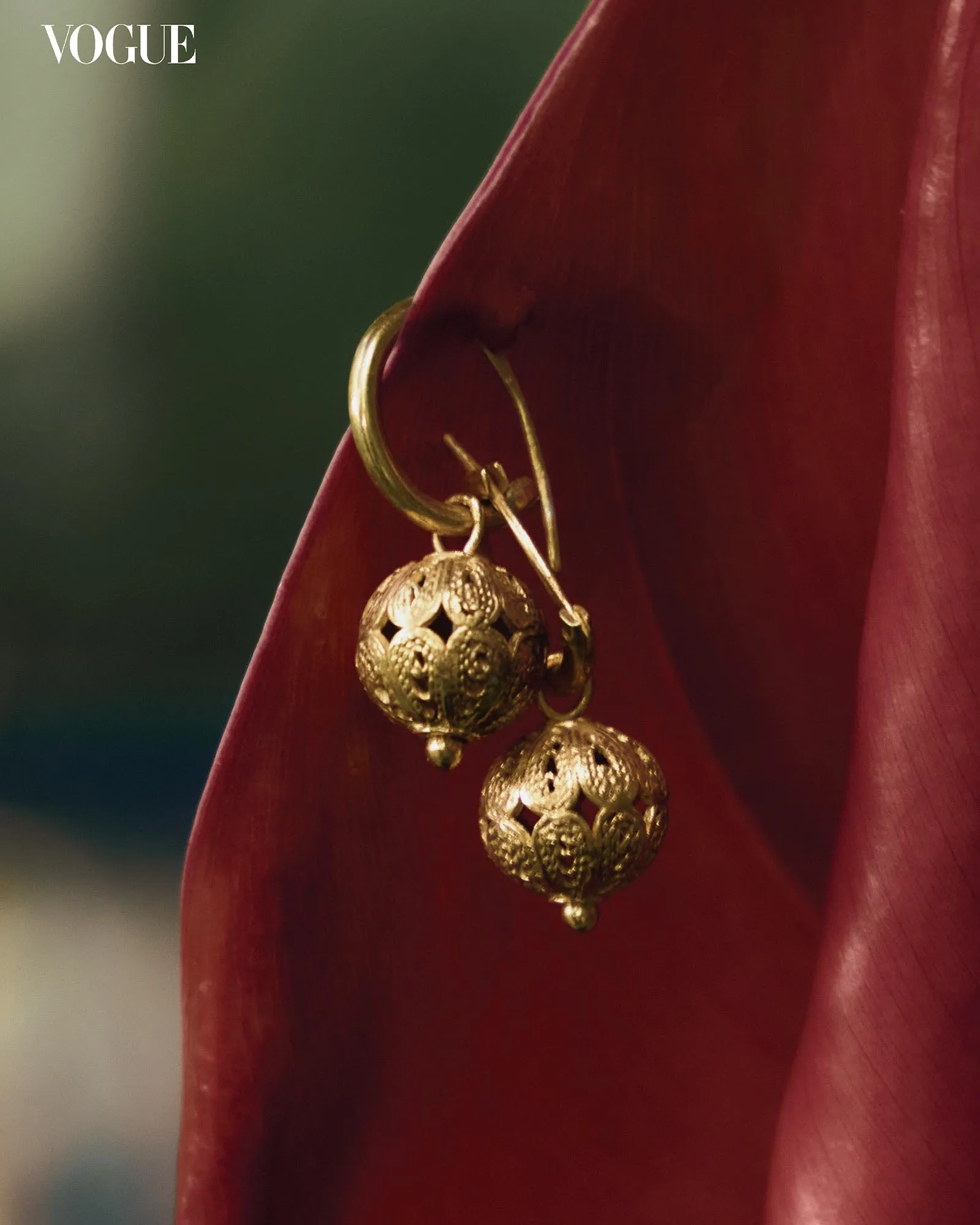 Vogue logo in top-left corner with gold-filigreed earrings hanging from red velvet fabric.