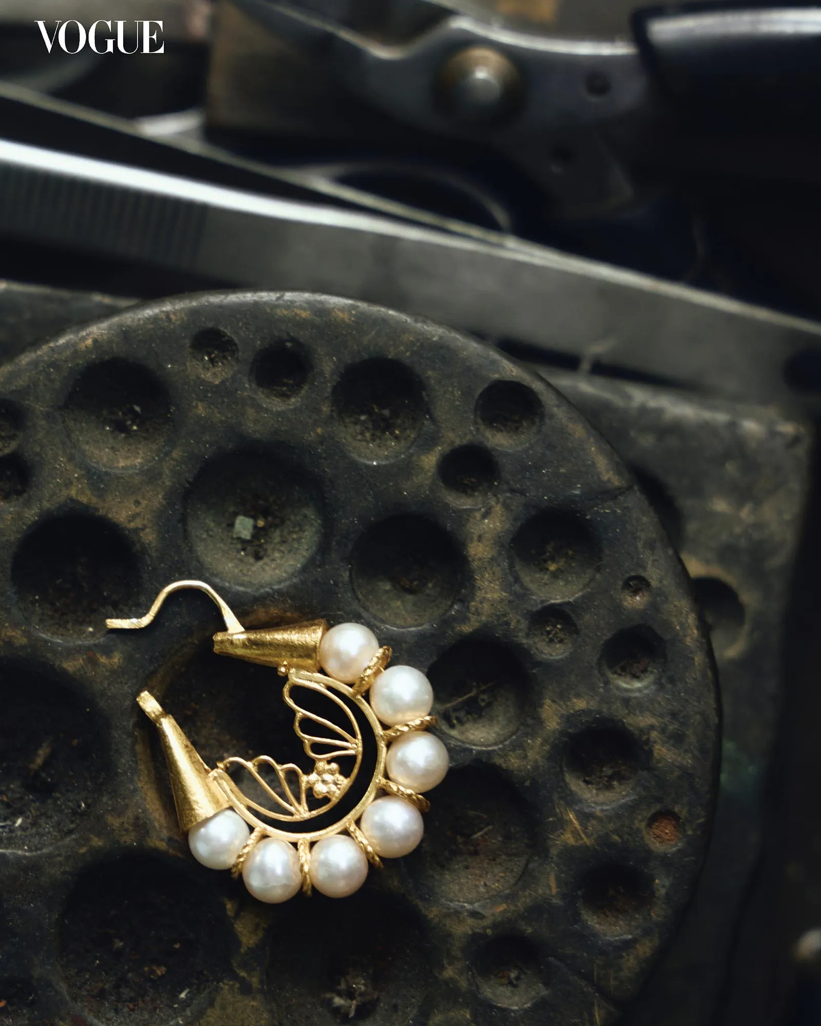 Close-up of a pearl bracelet with gold links on a dark, textured surface; Vogue logo in the corner.