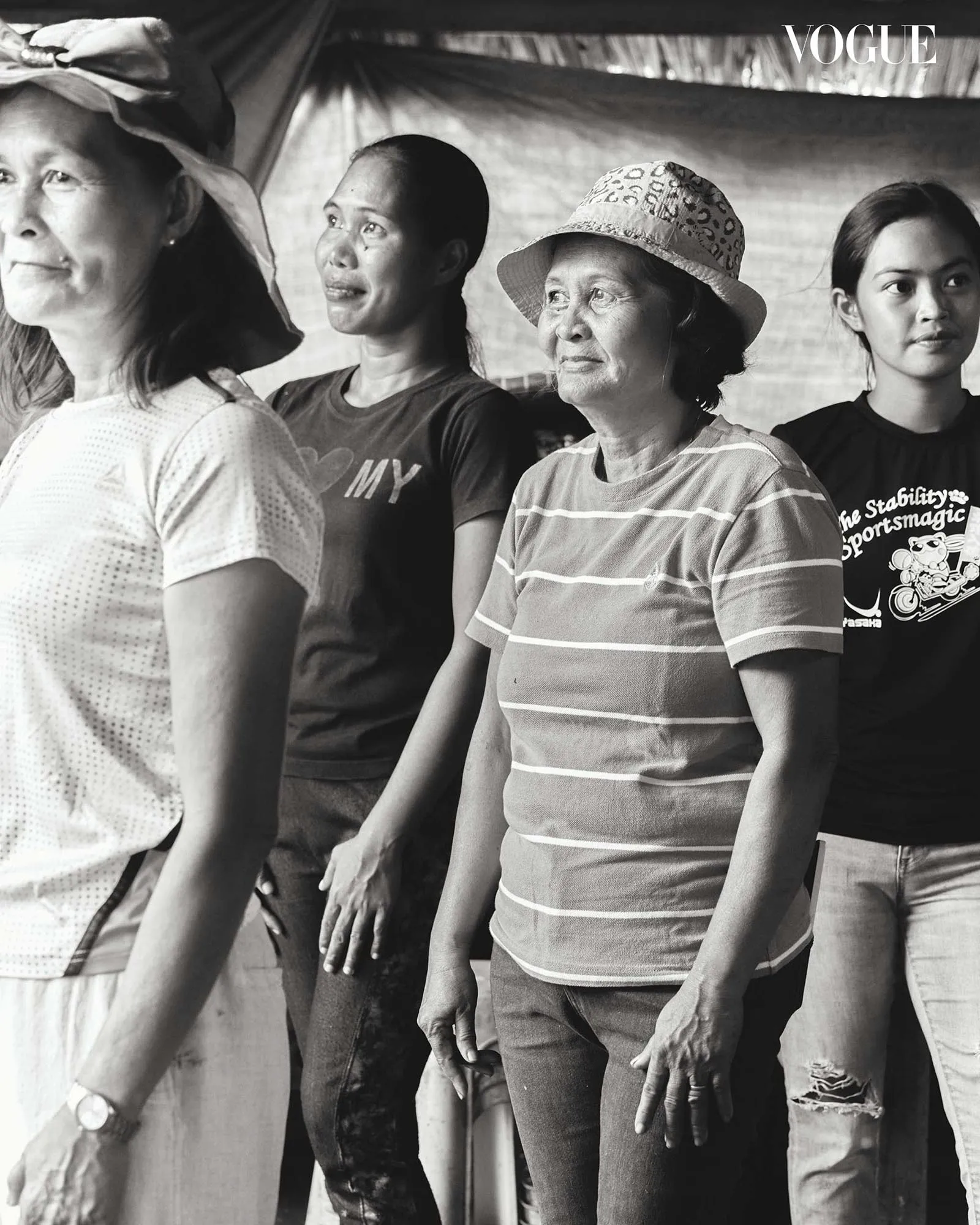 Four people stand in a line, looking to the right, in casual clothing; black-and-white Vogue photo.