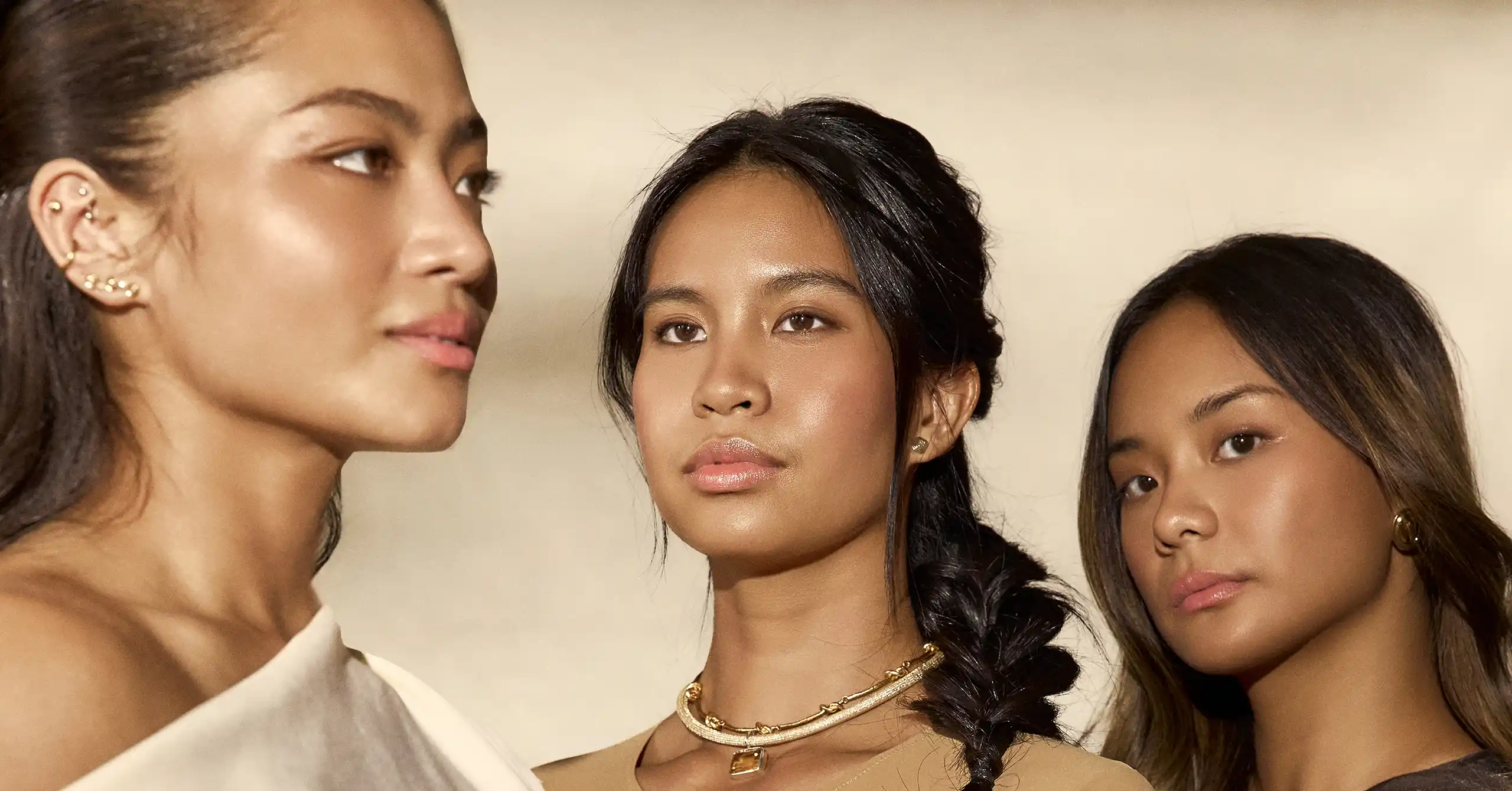 Three young women pose closely for a fashion shoot, each with braided hair and gold jewelry.