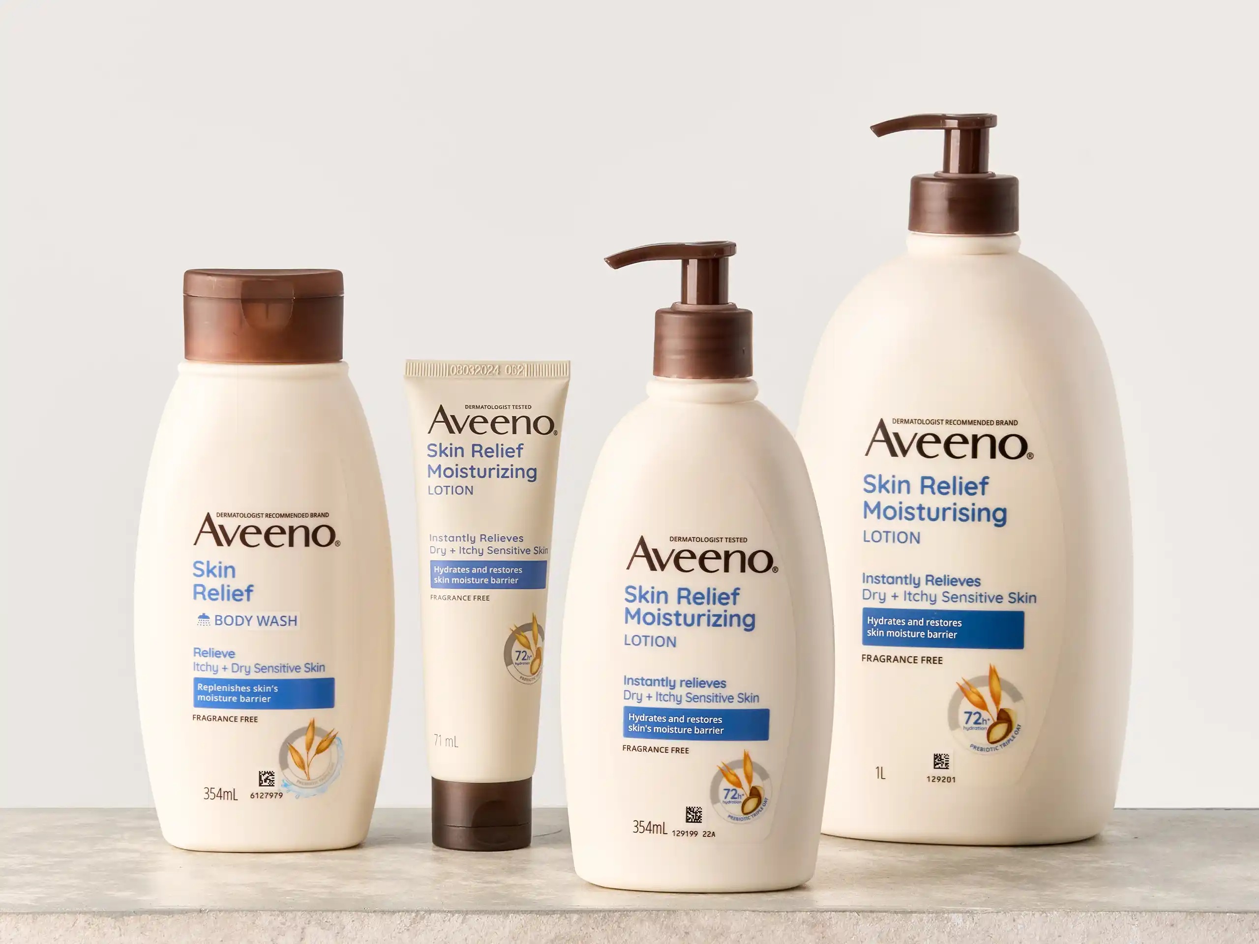 Row of Aveeno skin-relief lotion bottles with brown pumps on a neutral background, plus a small tube in the center flank.