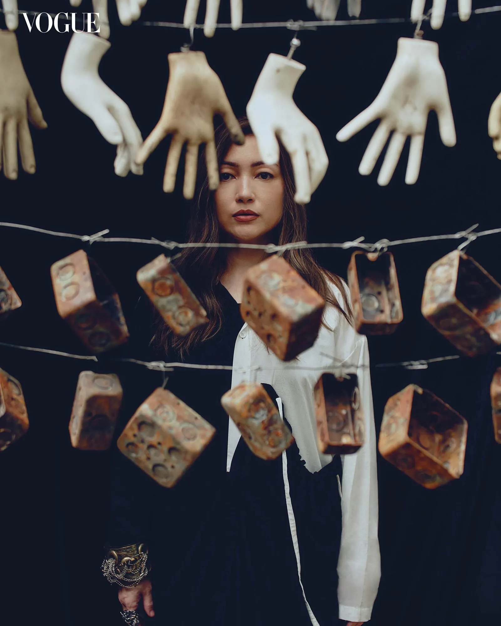Young woman stands behind a row of hanging vintage gloves and rusted metal tags on a wire, with a Vogue logo in the upper left corner.
