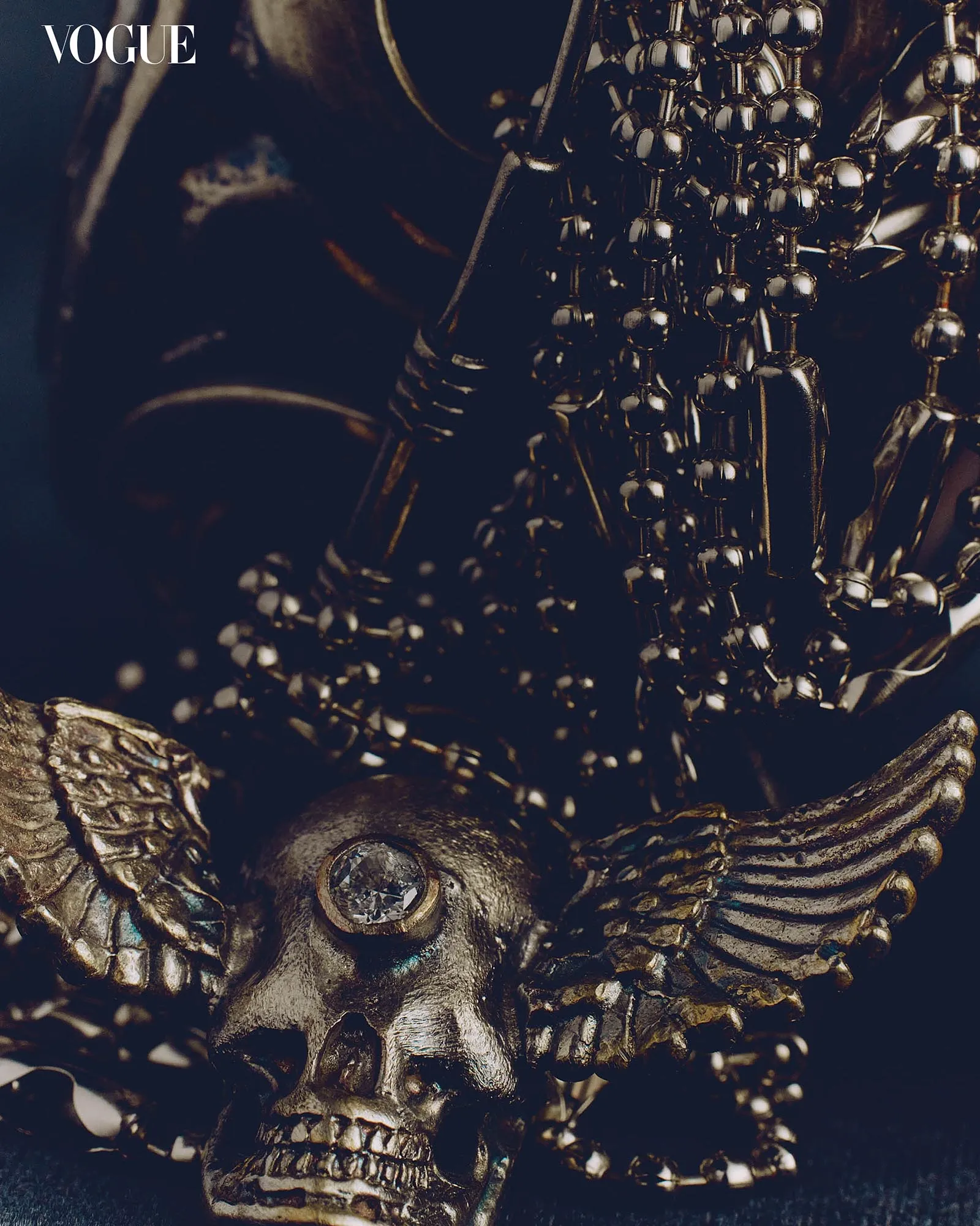 Close-up of dark metallic beaded jewelry draped over a decorative piece, with the Vogue logo in the upper left corner.
