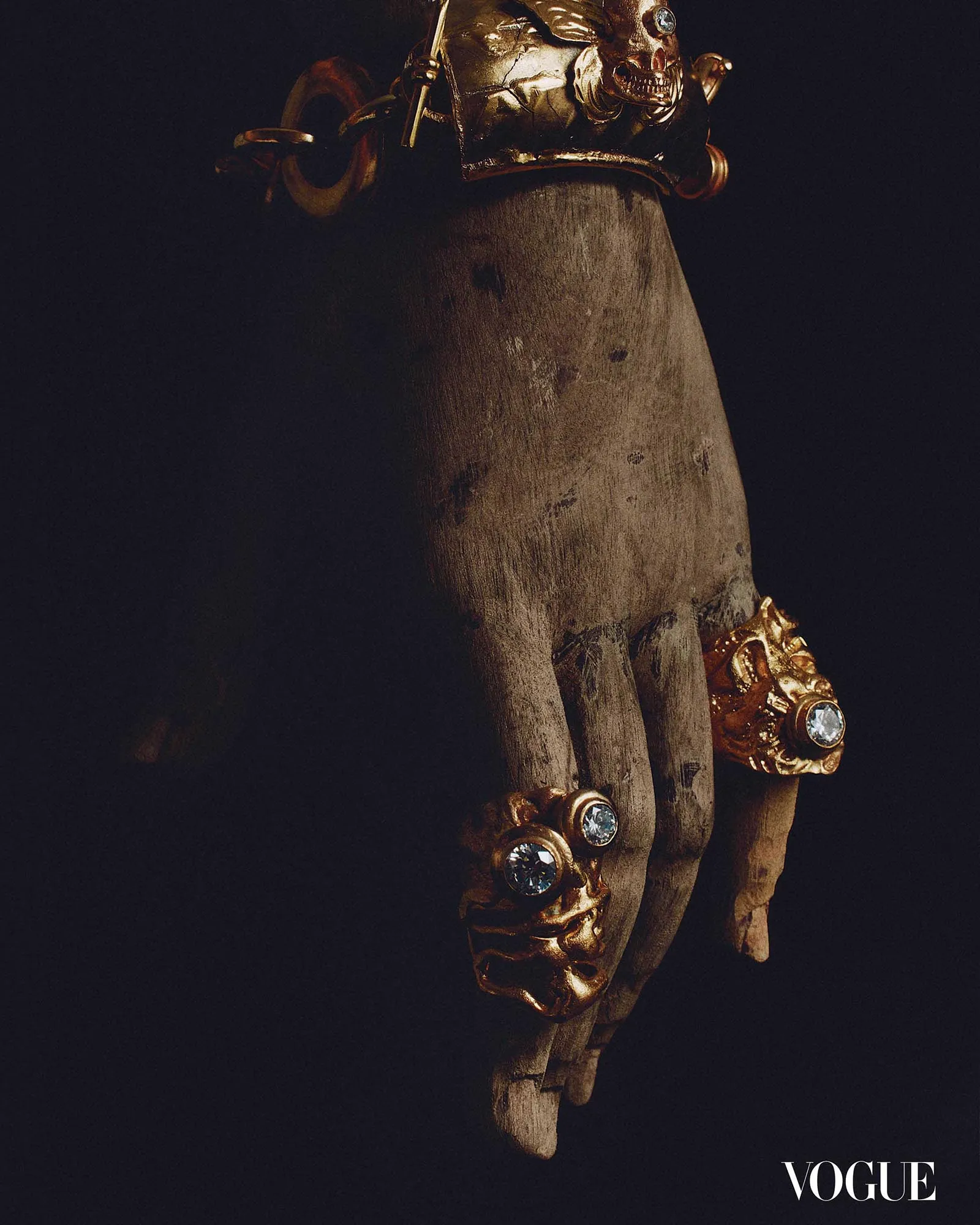 Decorative wooden hand wearing gold jewelry with diamonds on a dark background; Vogue watermark at bottom right.
