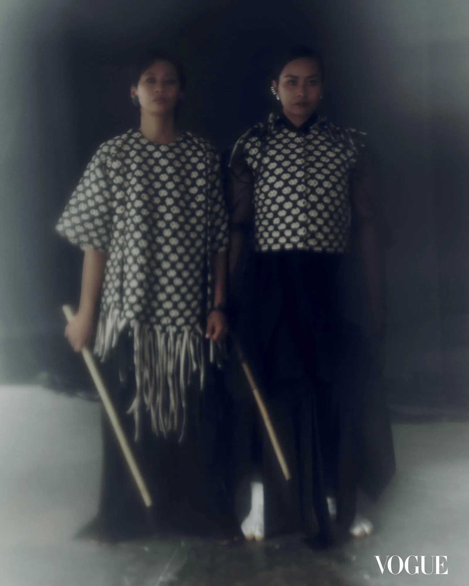 Two women in matching black-and-white floral dresses stand side by side; Vogue logo bottom right.