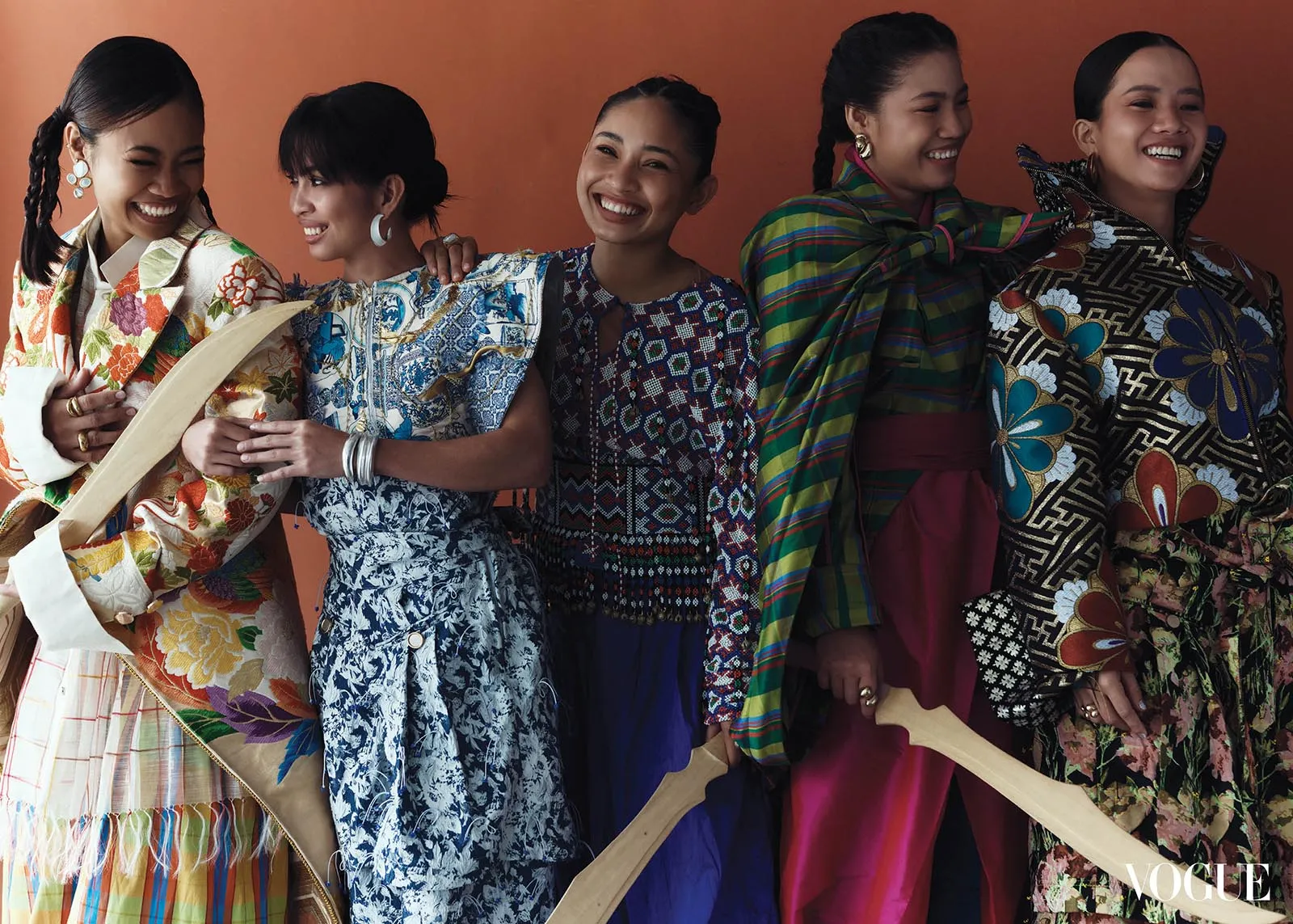 Five women in vibrant, patterned dresses posing together and smiling against an orange backdrop.