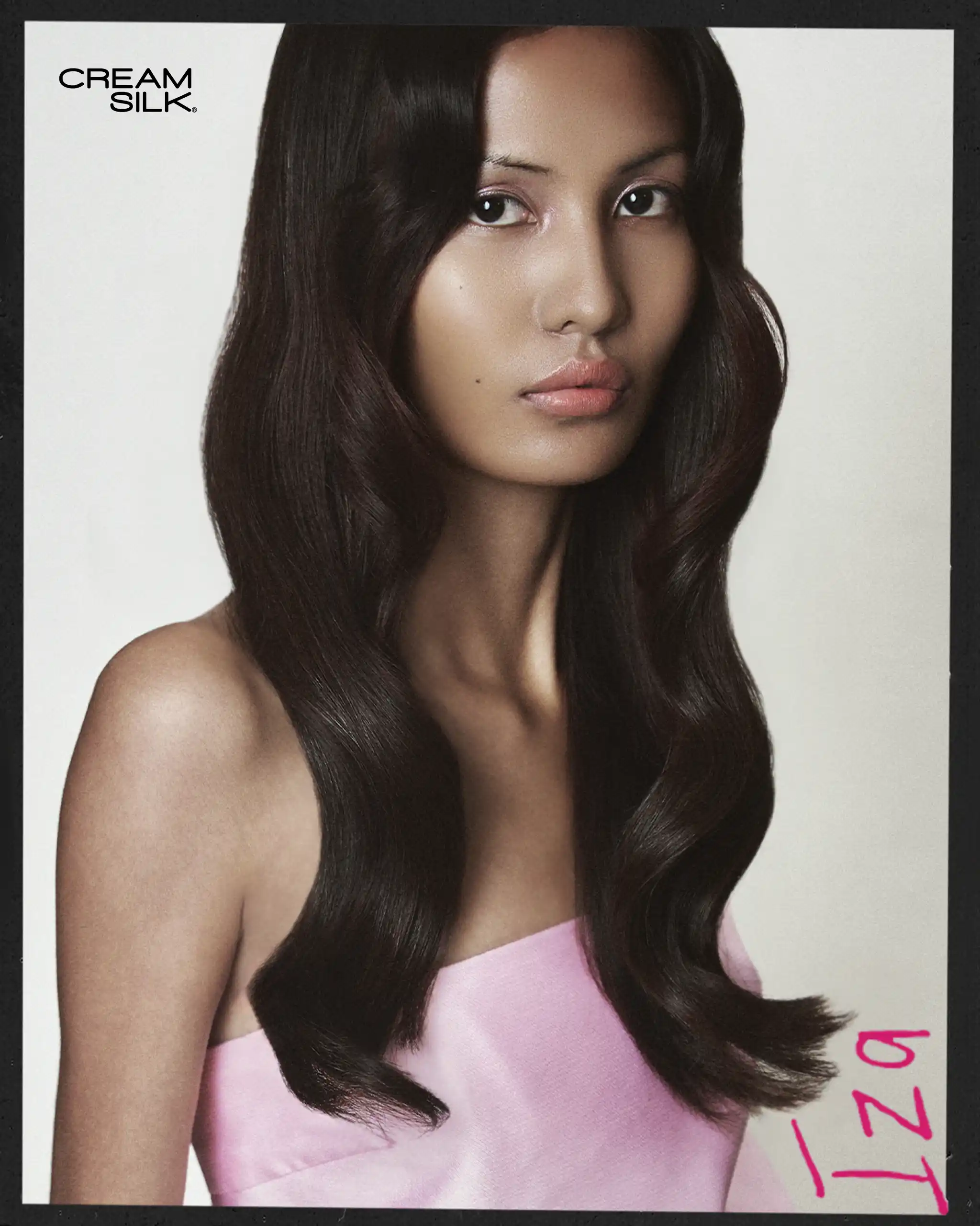 Model with long glossy dark hair wearing a pink strapless dress against a light background; Cream Silk logo in the top left corner.